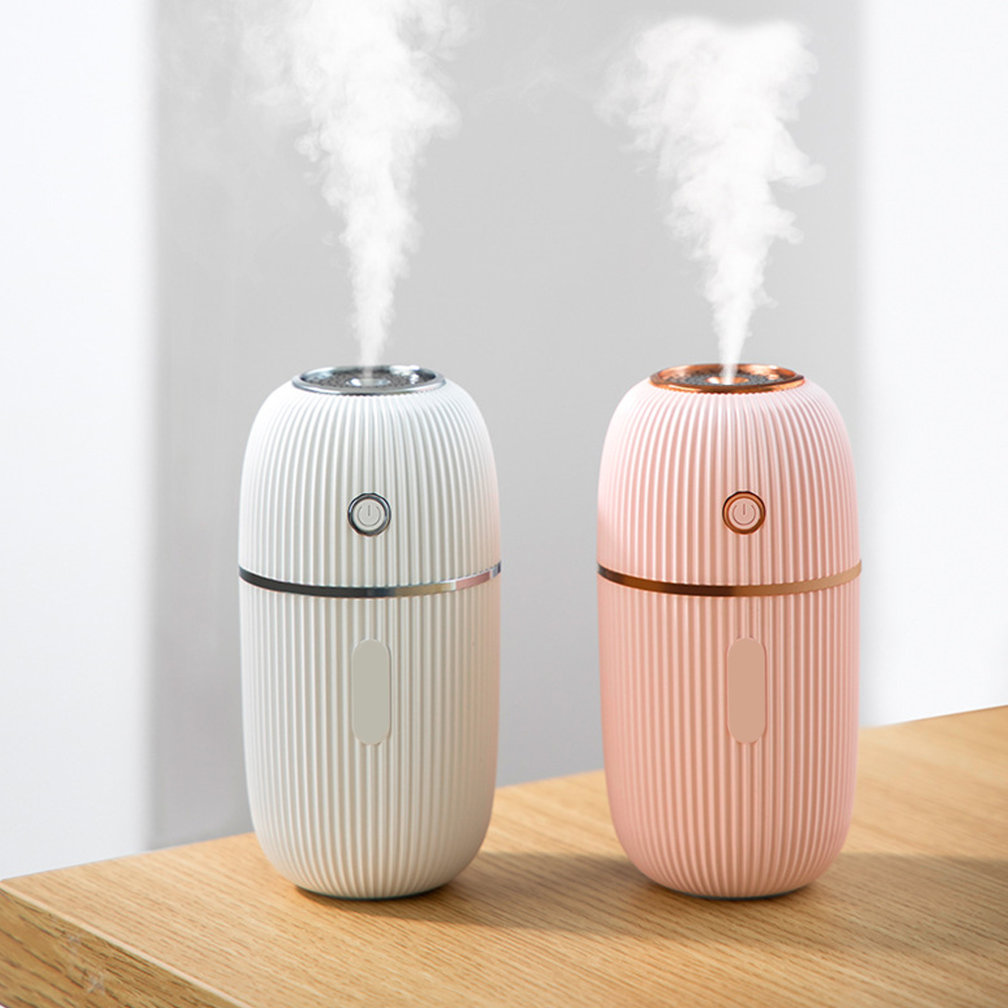 Zwei Humidifier, weiß und rosa, auf einem Holztisch, mit Dampf.
