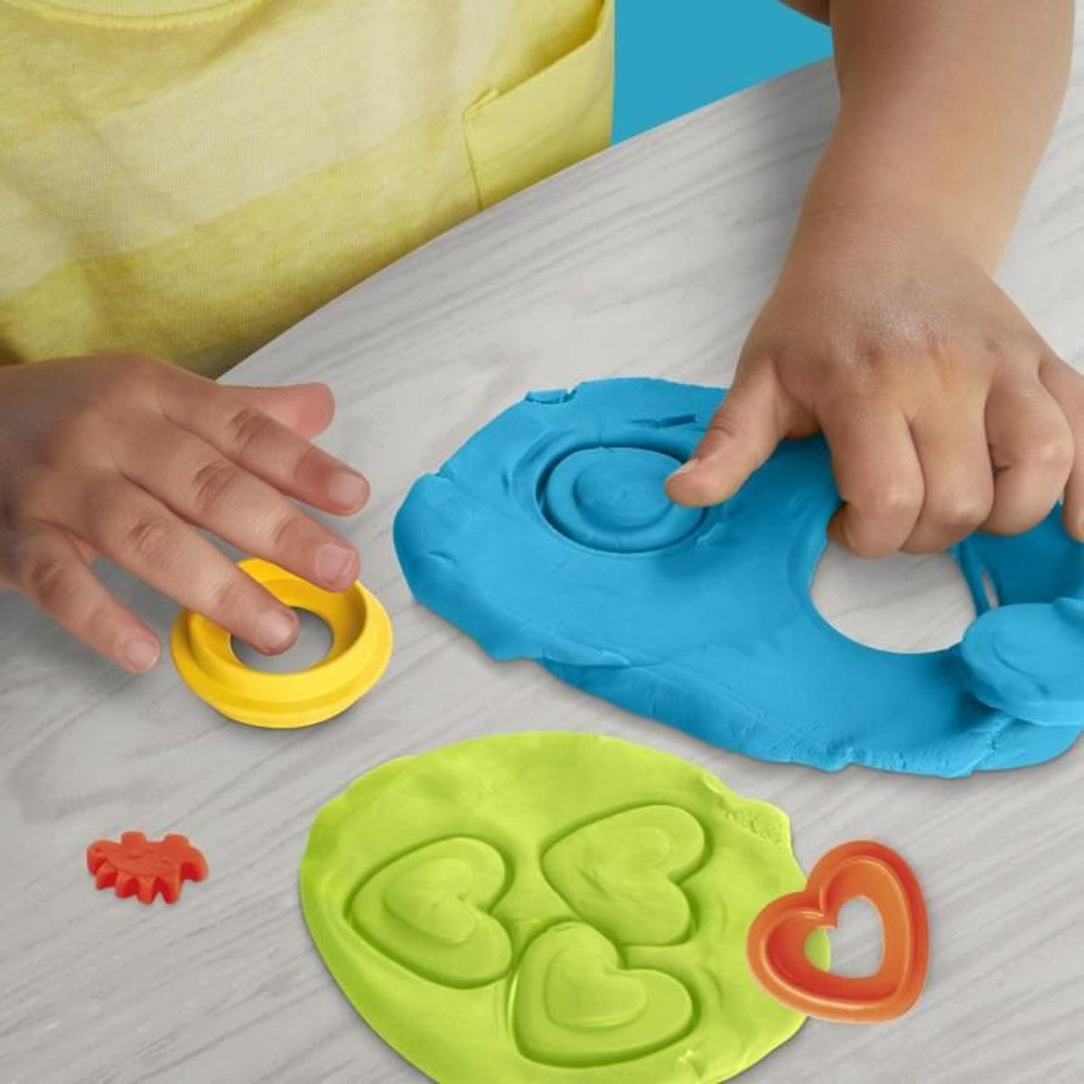 Un niño juega con plastilina azul y verde, haciendo formas de corazón con cortadores.
