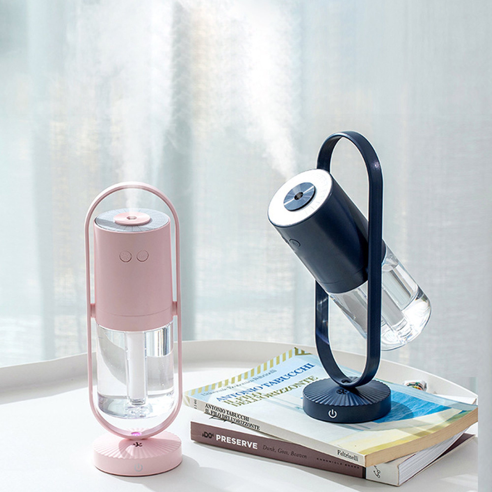 Zwei Luftbefeuchter, einer rosa, einer dunkelblau, sprühen Nebel, stehen auf Büchern.