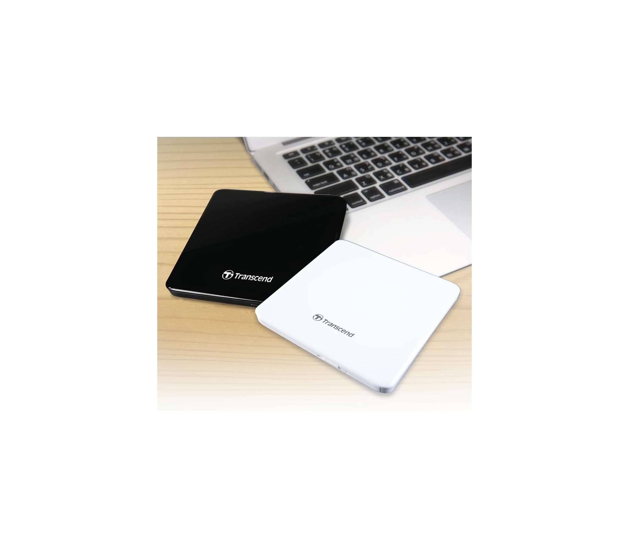 Zwei Transcend-Festplatten, schwarz und weiß, neben einem Laptop auf Holzhintergrund.