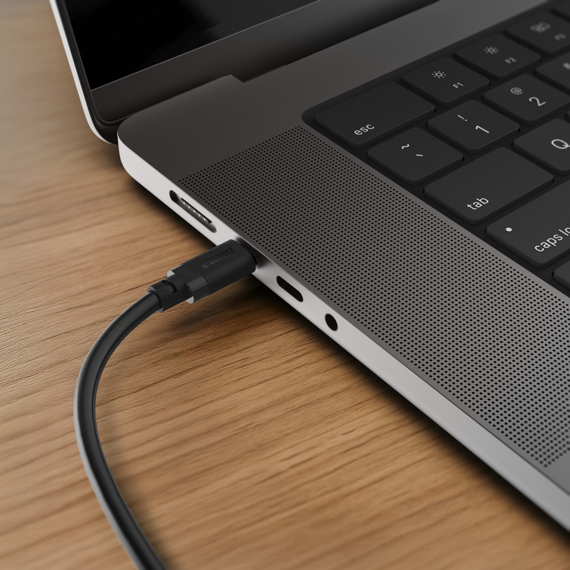 Ein schwarzes Kabel wird in einen Laptop eingesteckt, der auf einem Holztisch liegt.