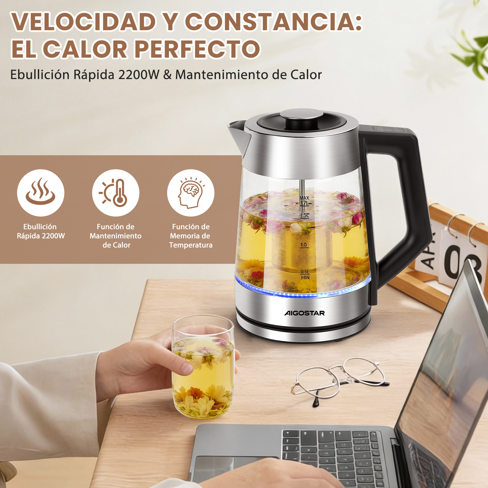 Un vaso de té junto a un hervidor, portátil y gafas en un escritorio.