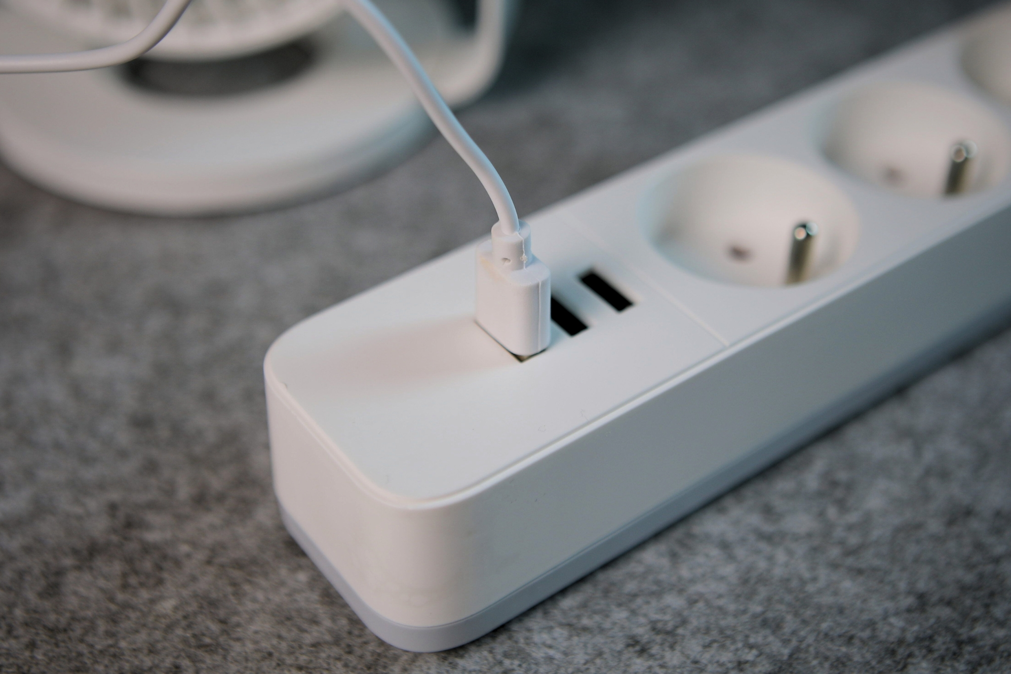 Biały kabel USB jest podłączony do białej listwy zasilającej z dwoma portami USB.