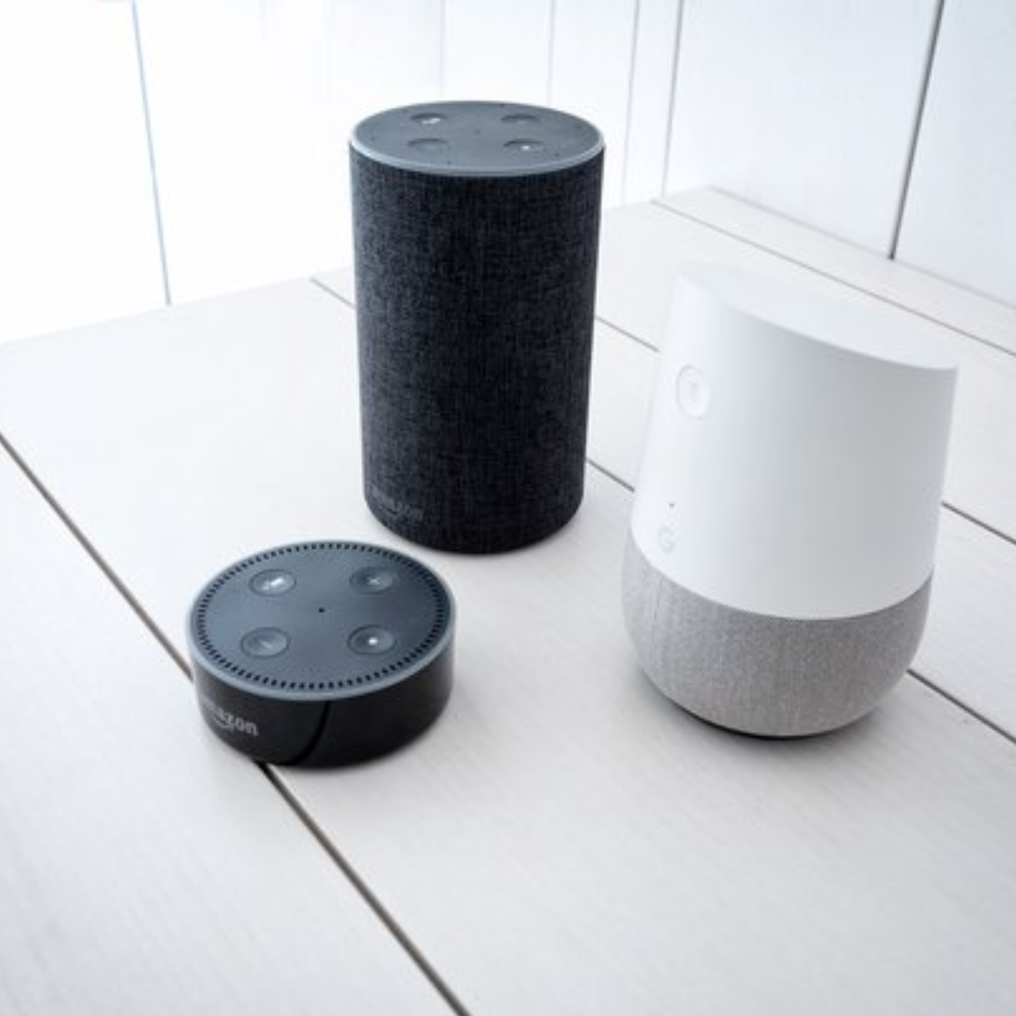 Drie slimme luidsprekers: twee zwarte Amazon-apparaten en één witte Google Home.