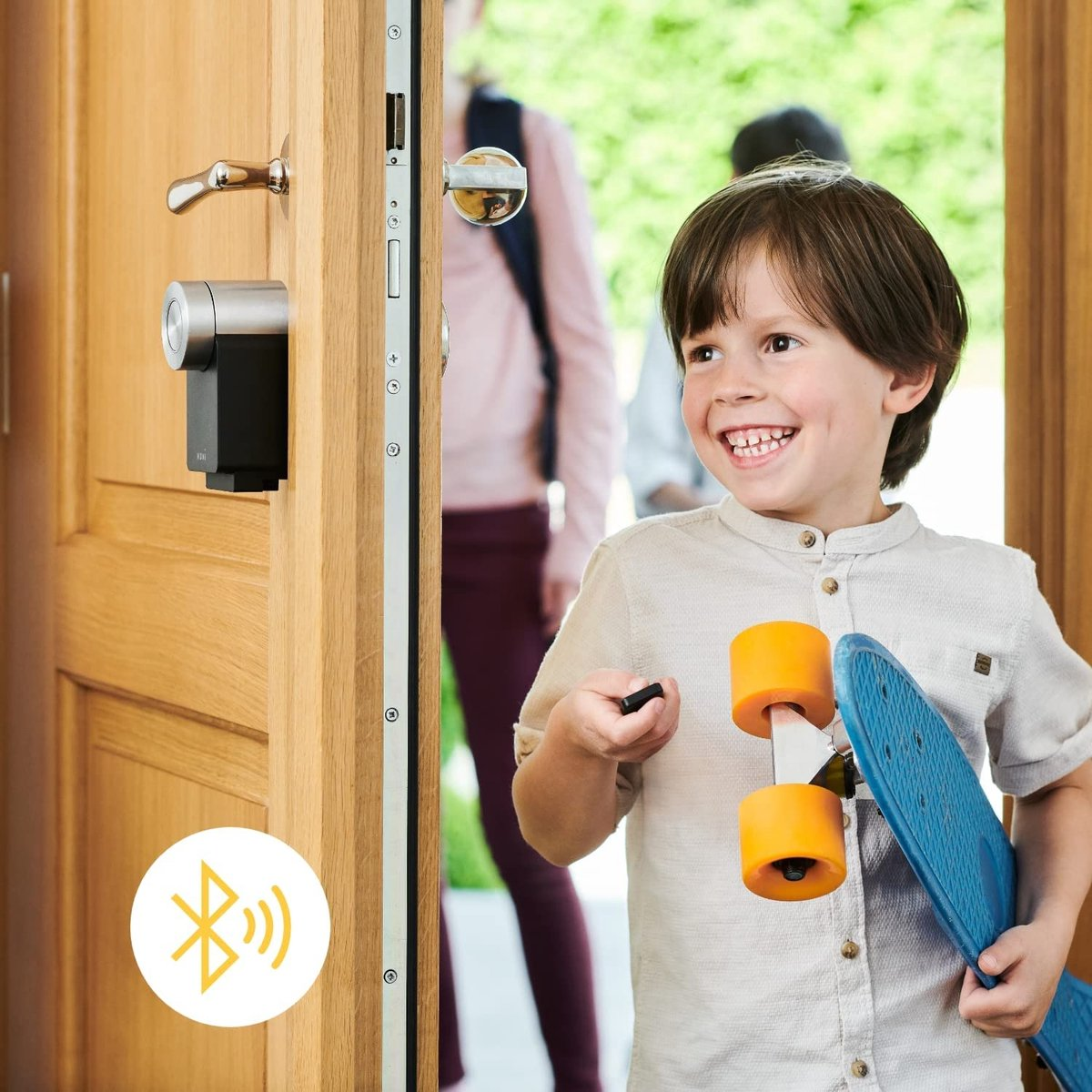 Boy with skateboard holds key in front of open door, family in background.