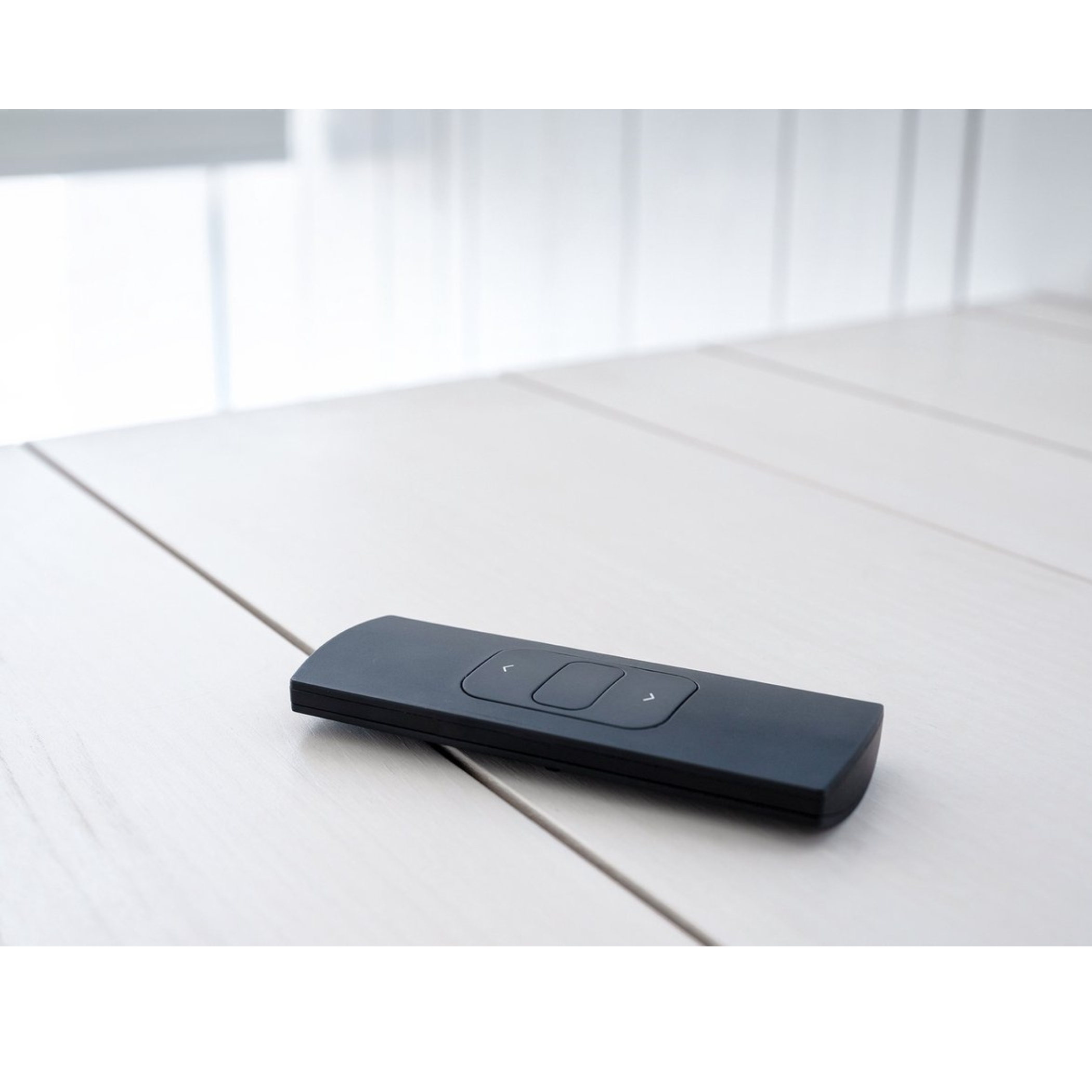 A black remote control on a light-colored wooden table.
