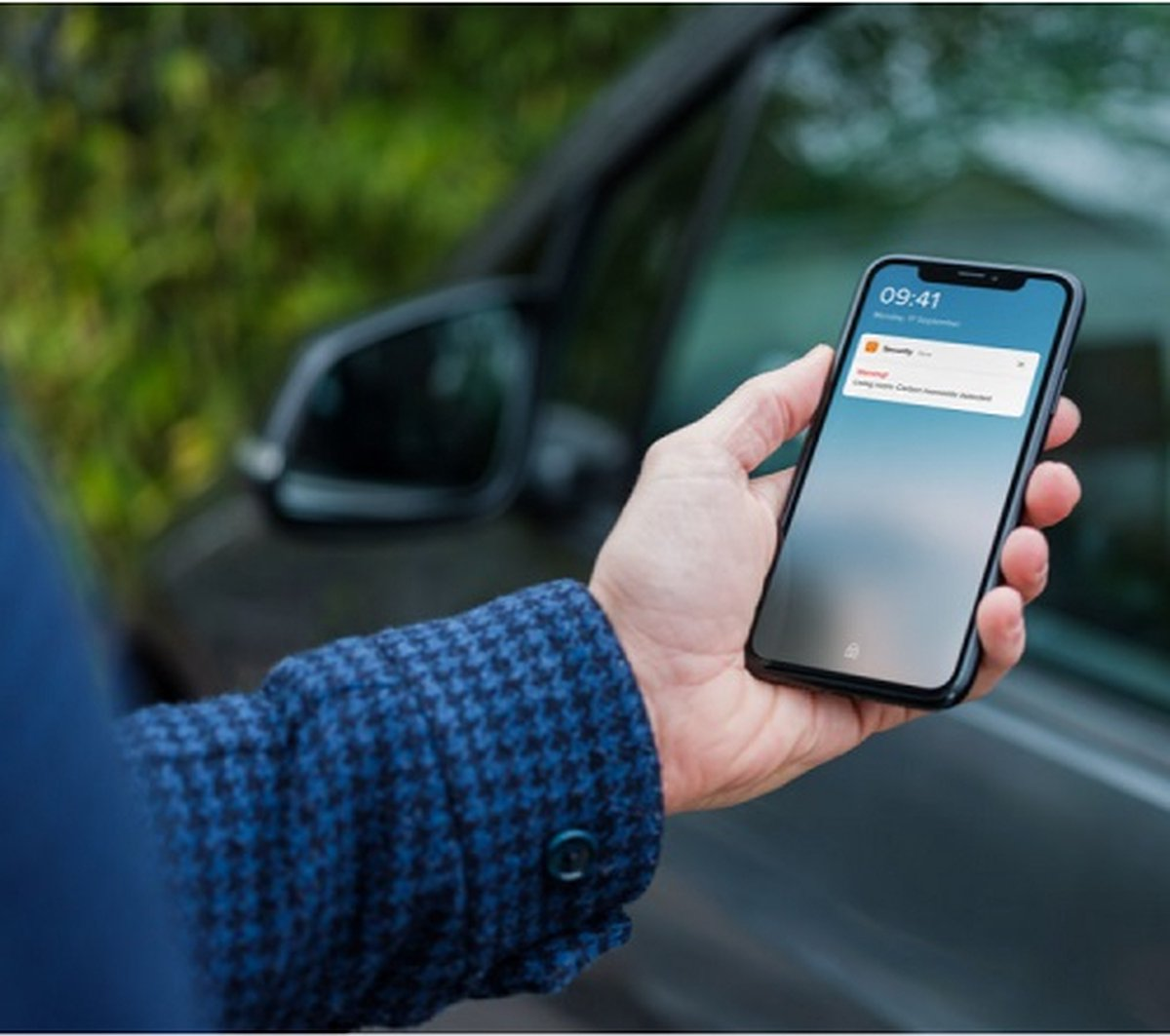 Man houdt smartphone naast auto. Waarschuwing: Koolmonoxide gedetecteerd.