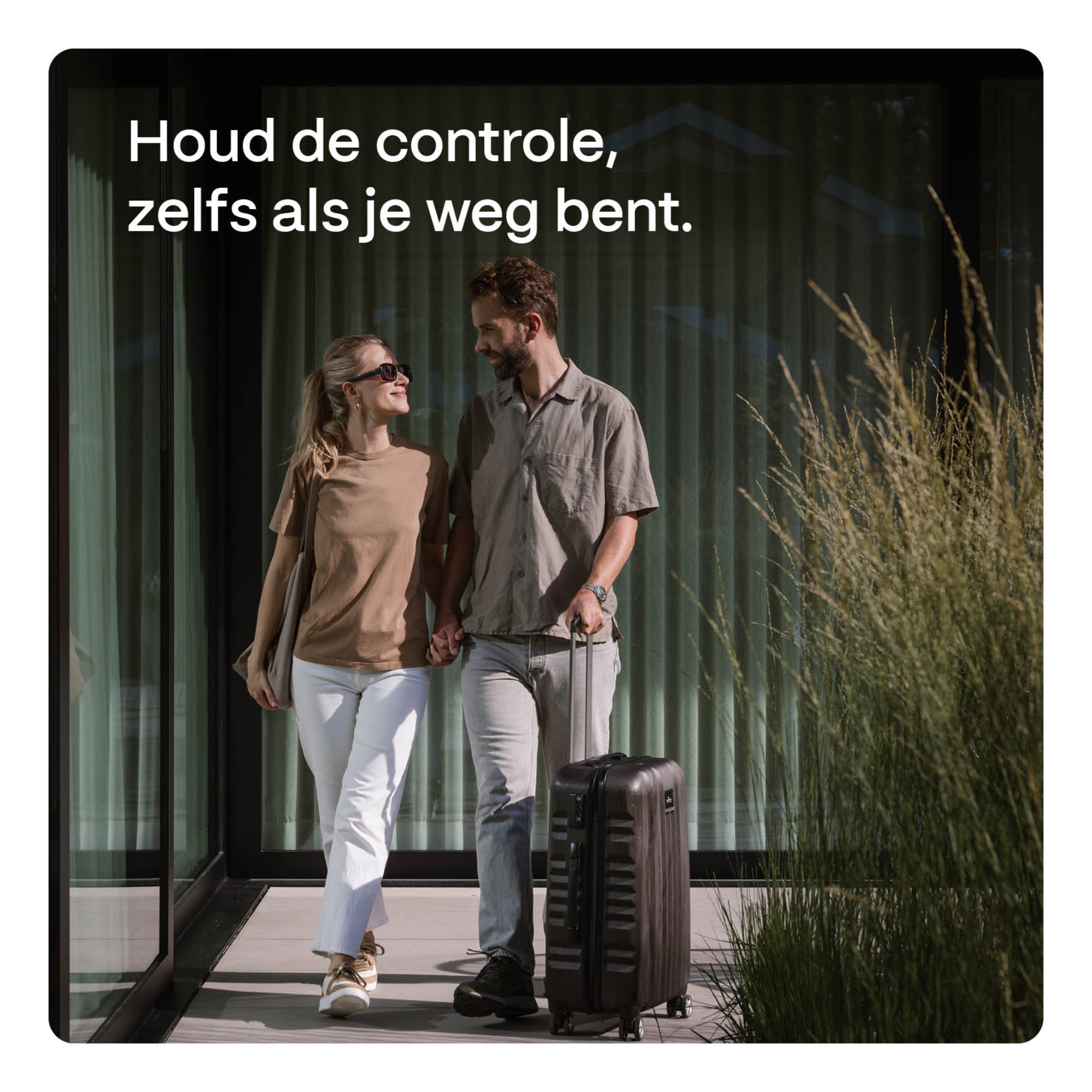 A man and woman hold hands, walking with a suitcase in front of a modern house.