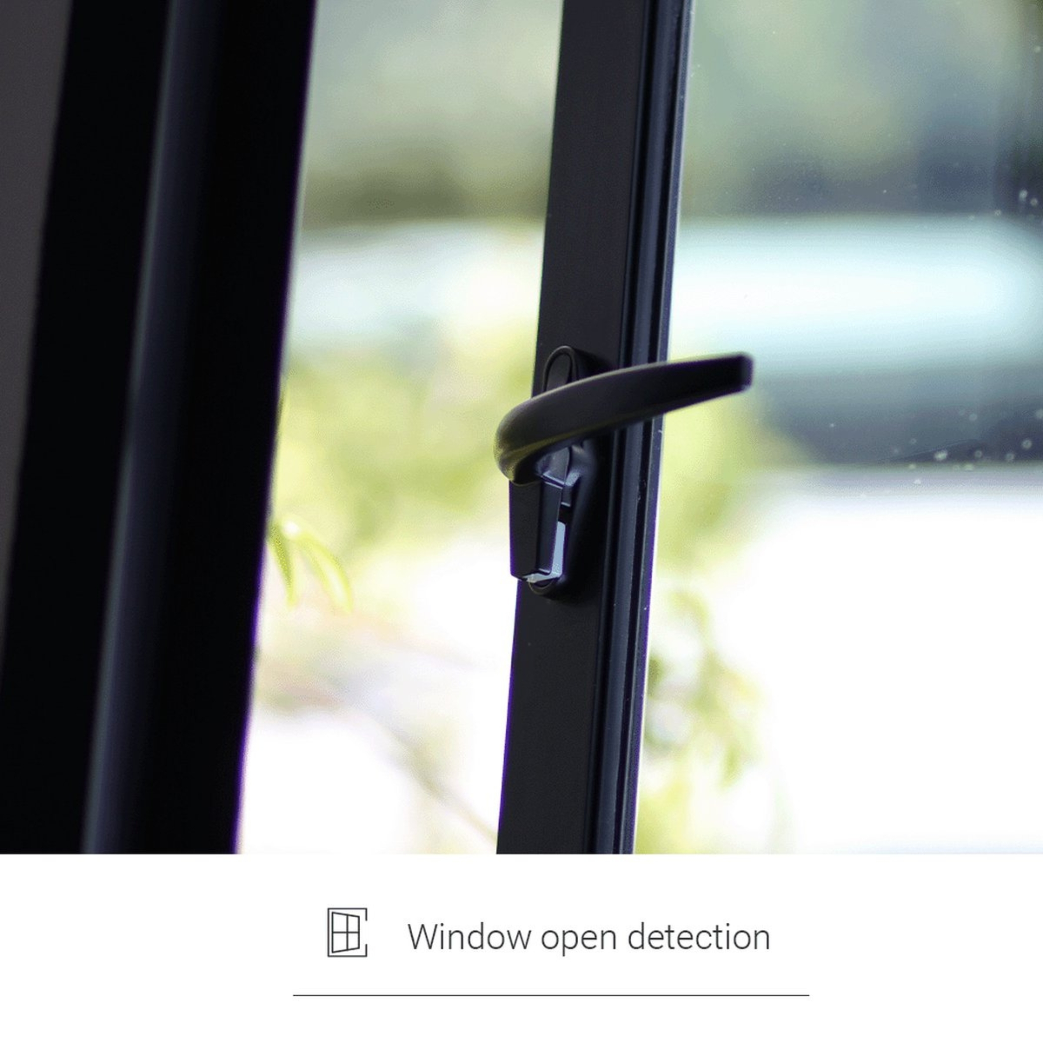 Black window handle with locking mechanism against a blurred green background.