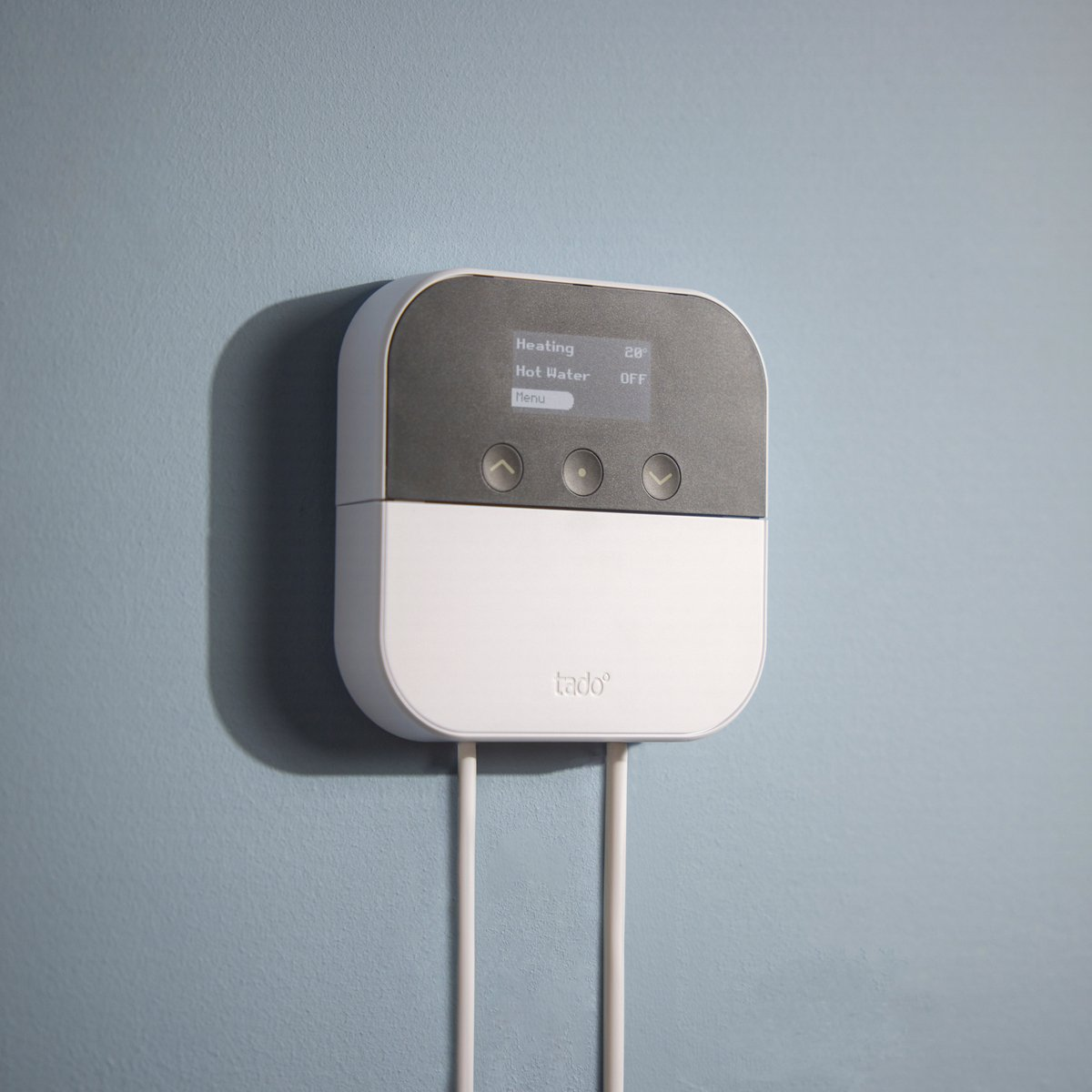 A white Tado device with a dark screen is mounted on a blue wall.