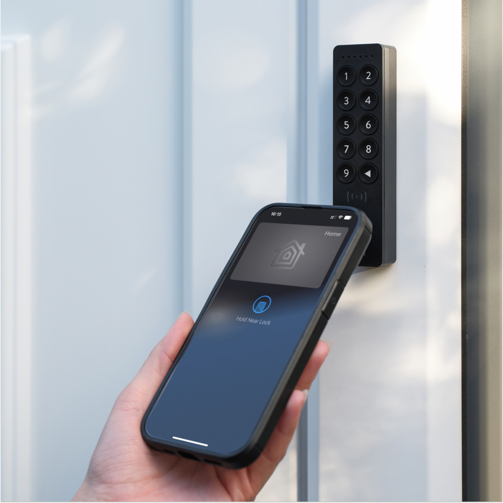 Een hand houdt een smartphone vast bij een digitaal toetsenbord slot op een witte deur.