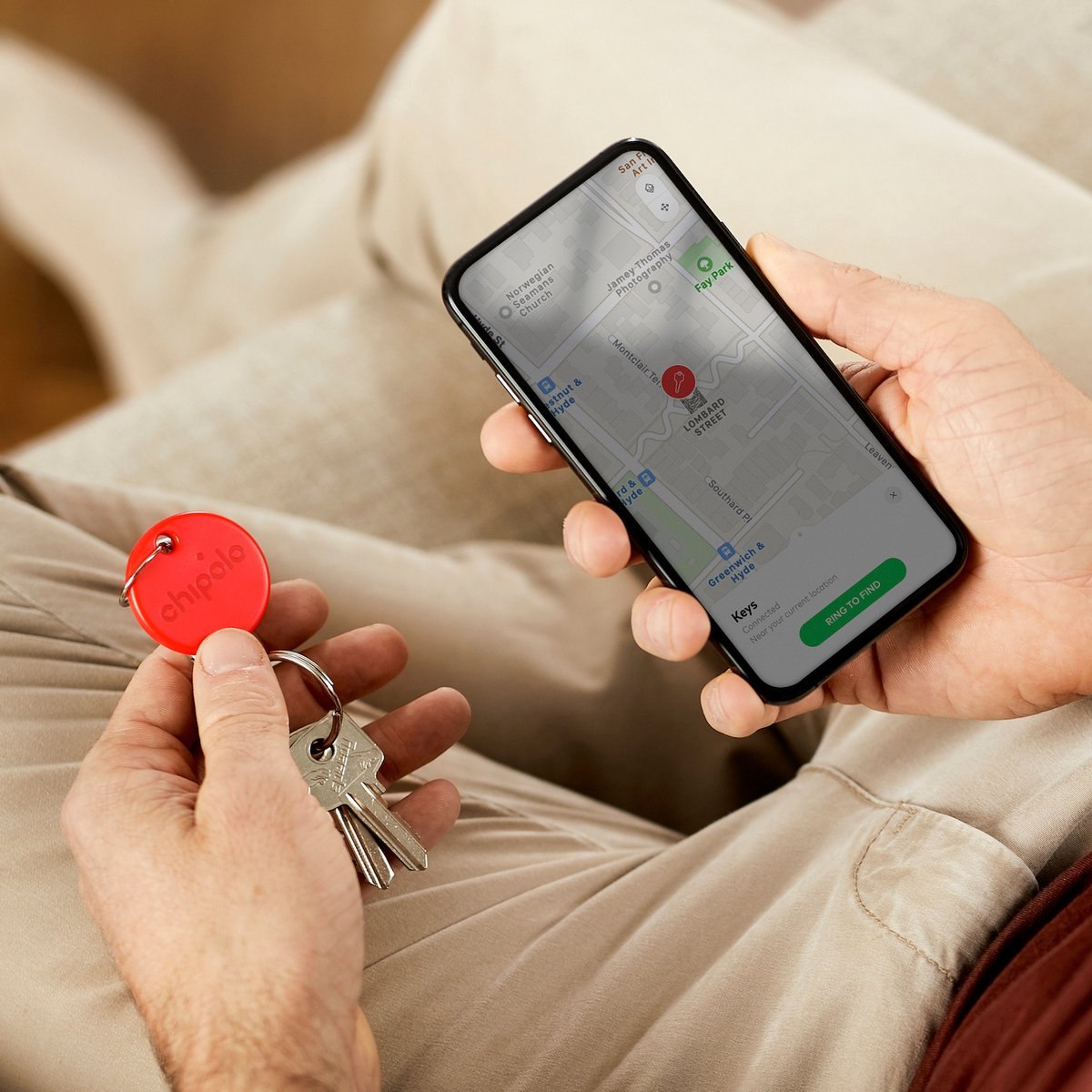 Handen houden een Chipolo sleutelhanger en smartphone met kaart vast.
