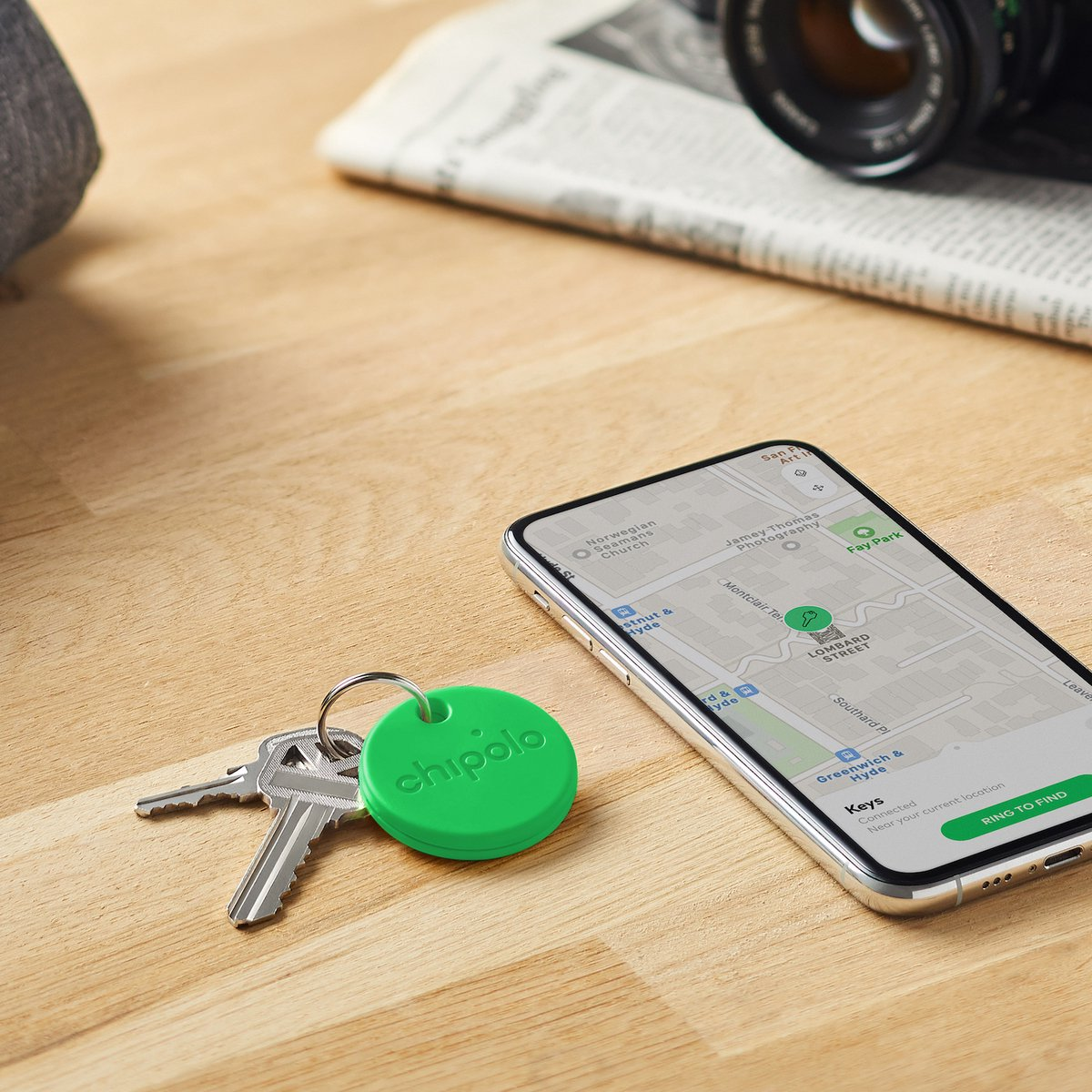 Een groene Chipolo tracker en sleutels naast een smartphone met kaart.