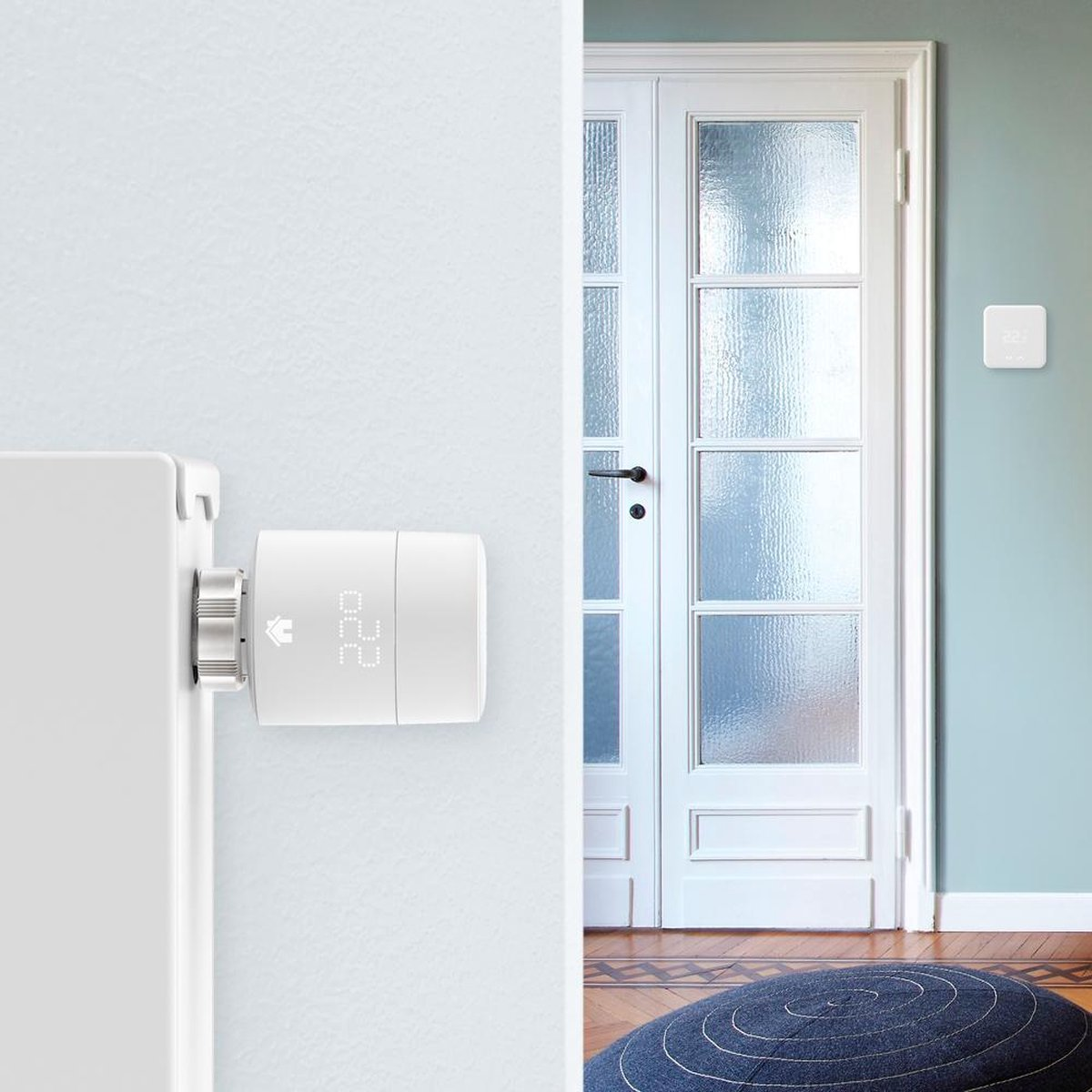 A white thermostat is attached to a radiator. Next to it is a door.