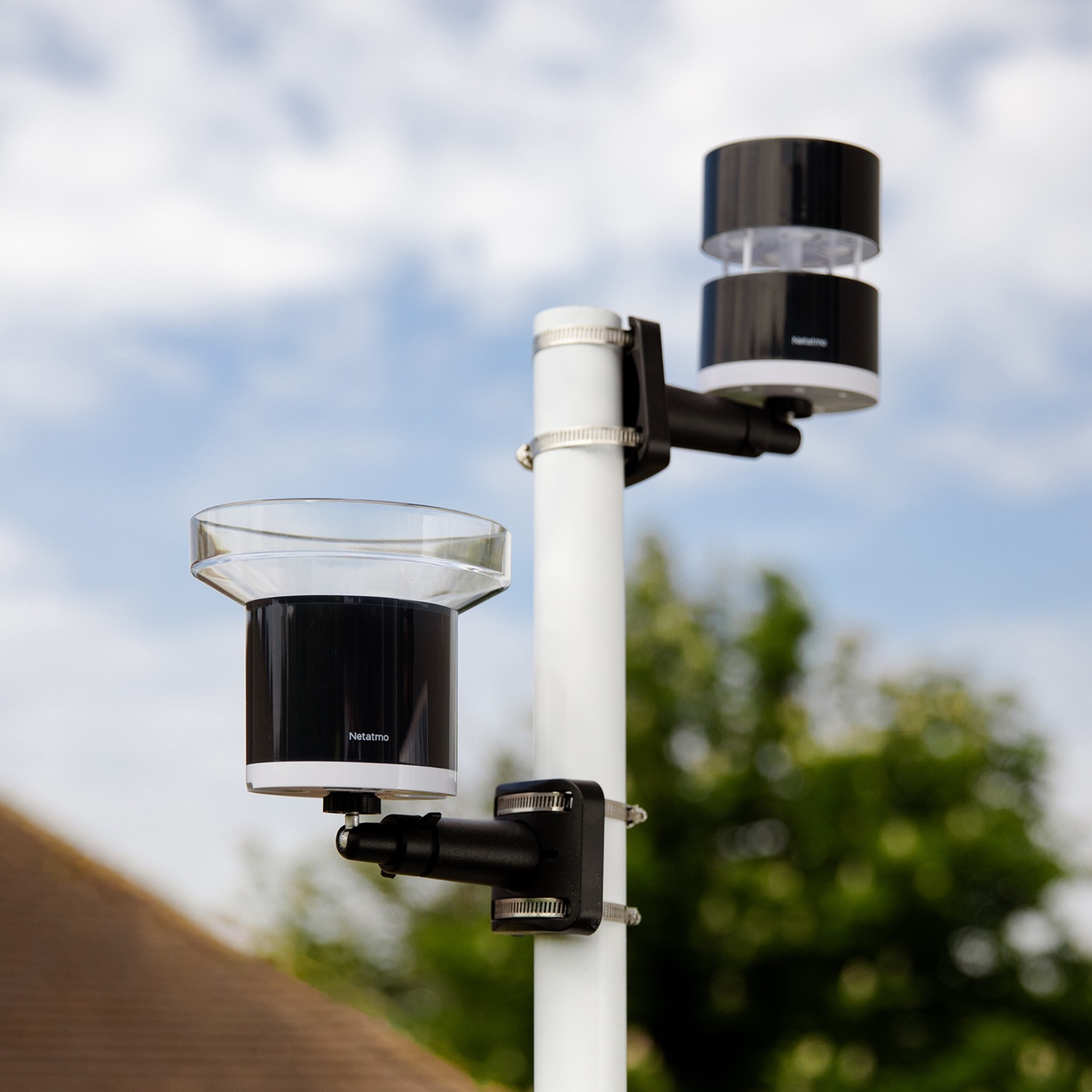A weather station with rain gauge and anemometer on a pole against a blue sky.