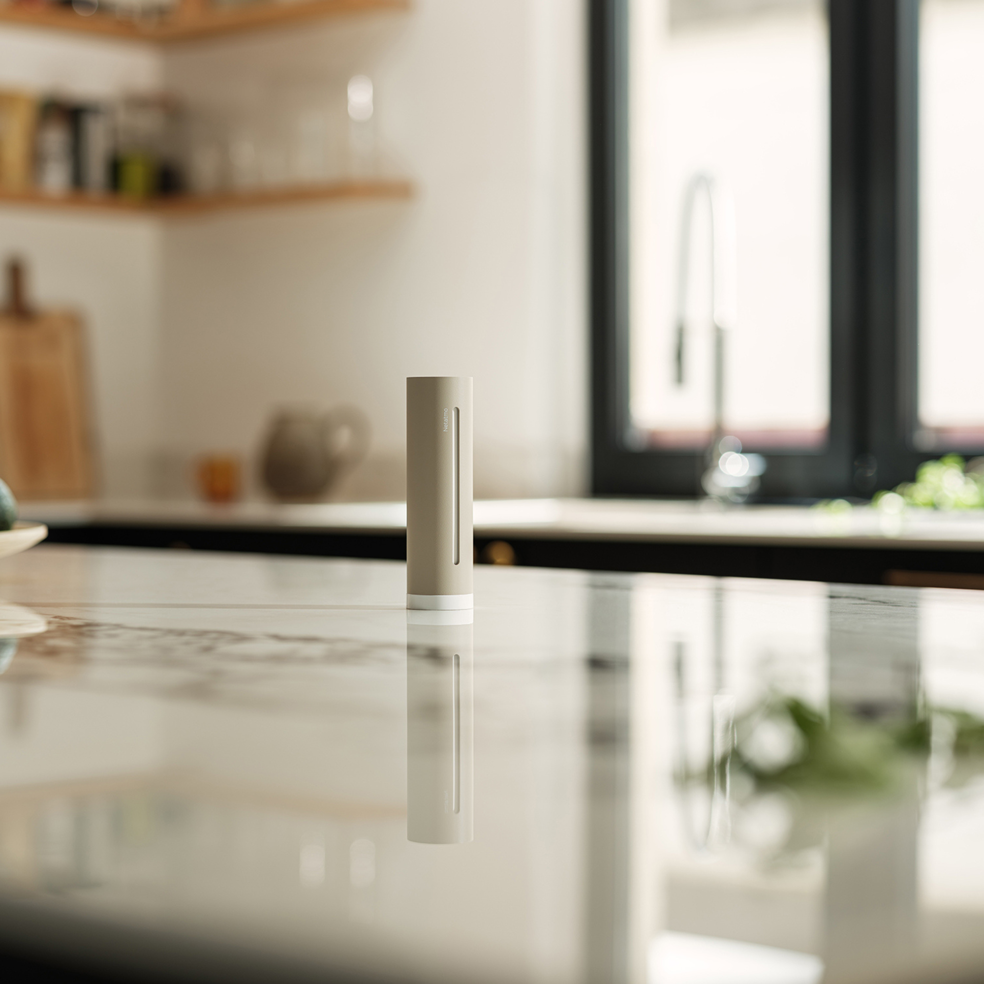 A gray cylinder sits on a marble counter in a kitchen. Shelves and a window are visible.