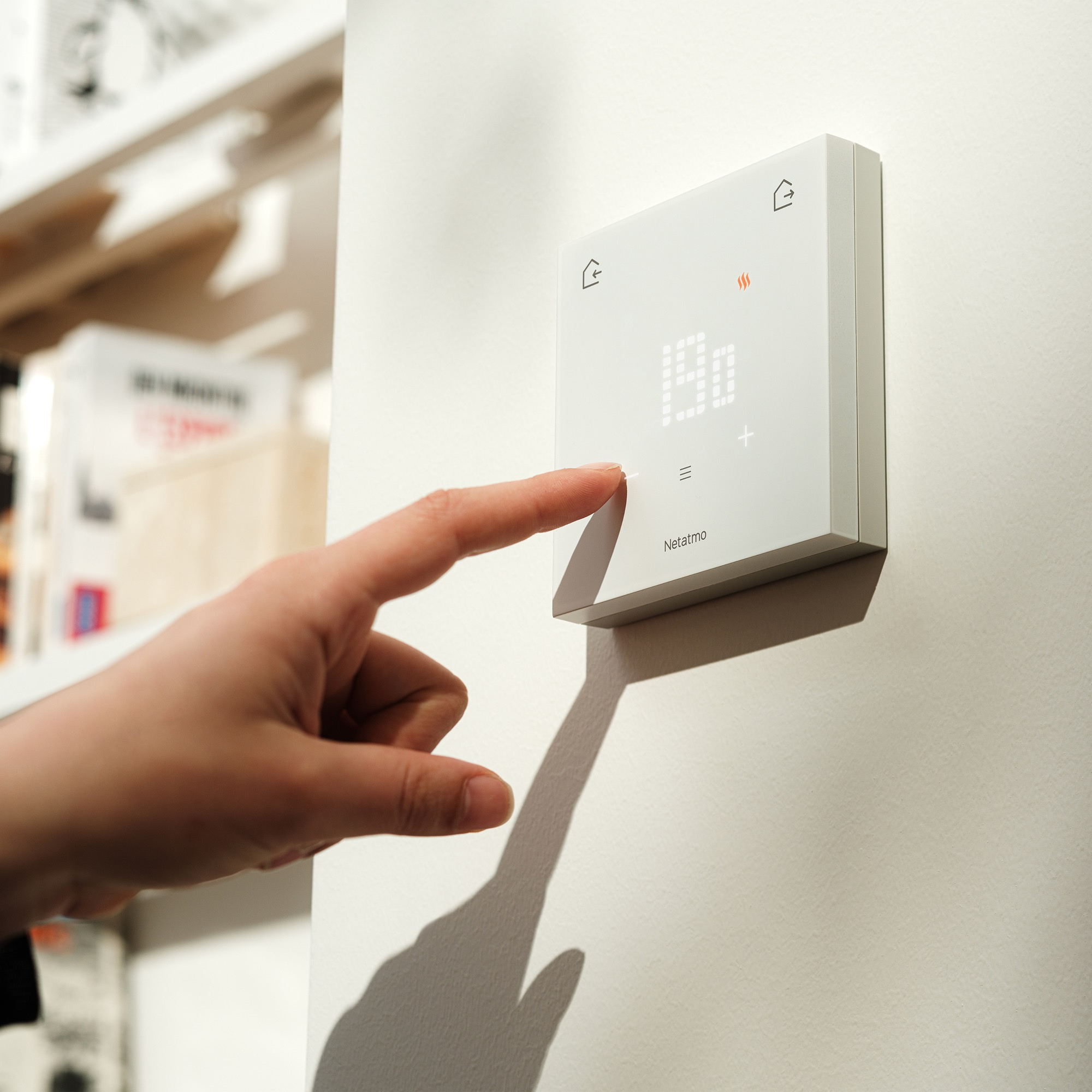 Une main touche un thermostat blanc avec un écran numérique.
