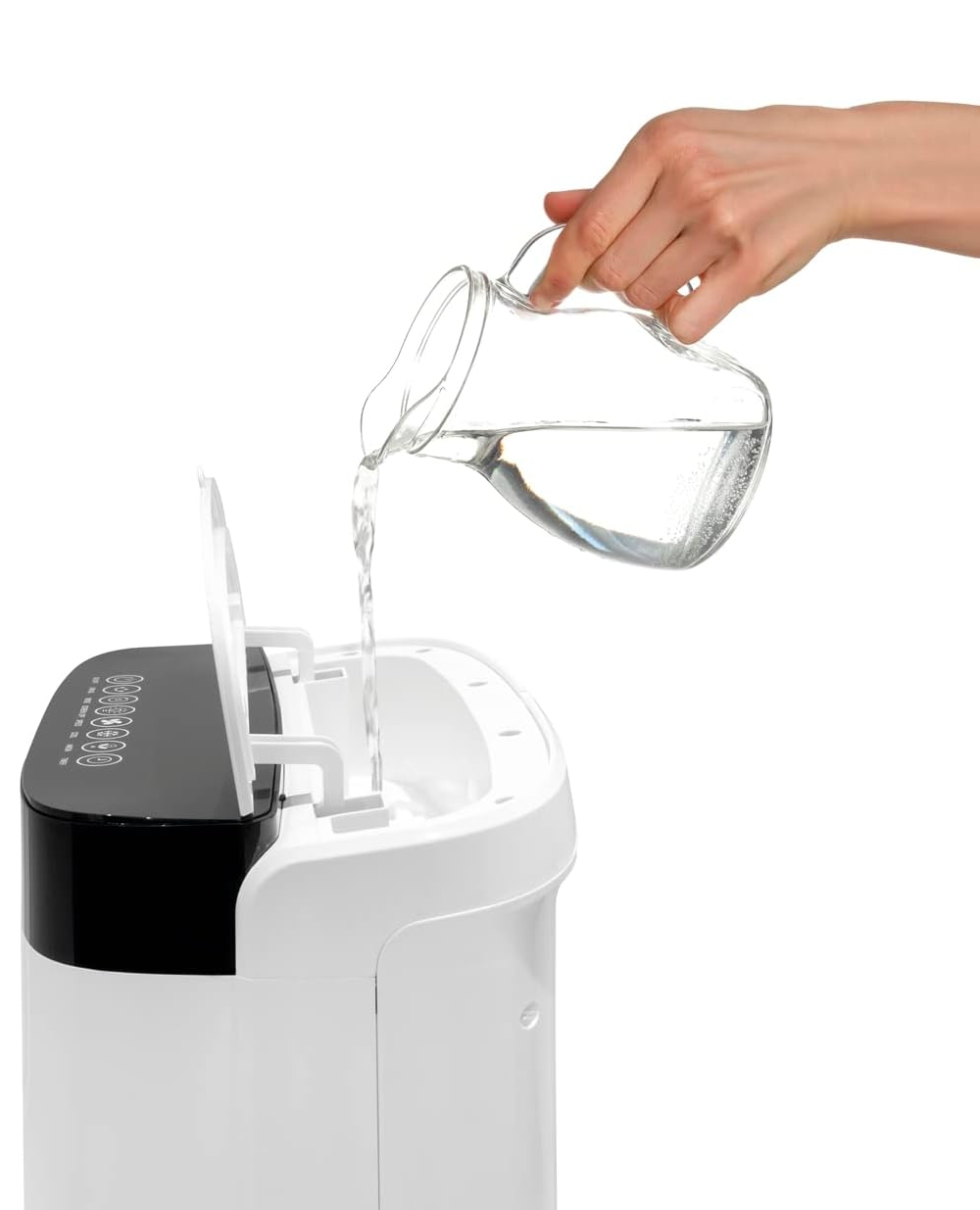 Una mano versa acqua da una brocca di vetro in un apparecchio bianco con coperchio nero.