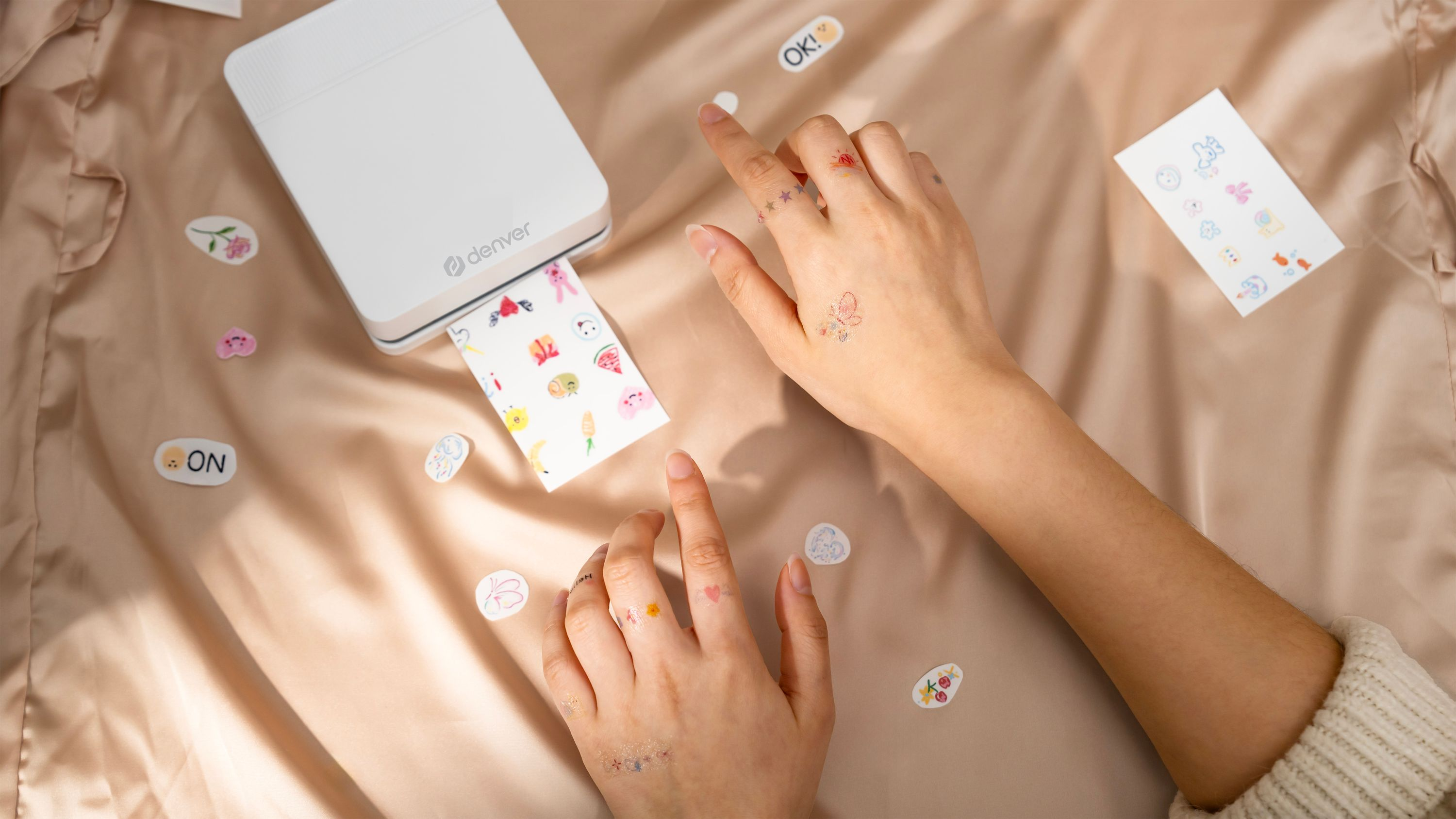 Ein weißer Drucker druckt temporäre Tattoos auf eine glänzende Stoffoberfläche.