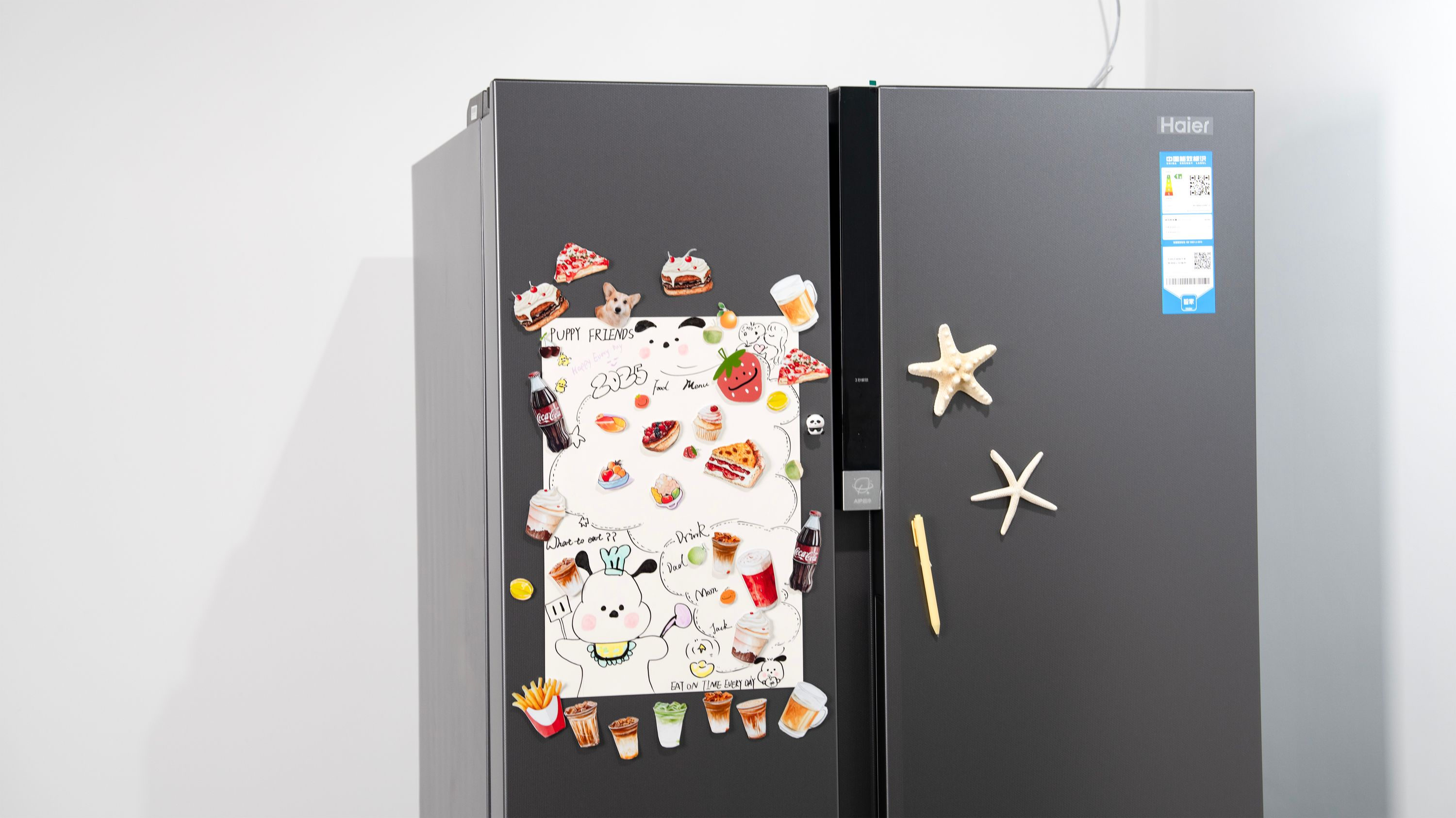 Ein dunkelgrauer Haier-Kühlschrank mit Magneten: Essen, Getränke und eine Hundezeichnung.