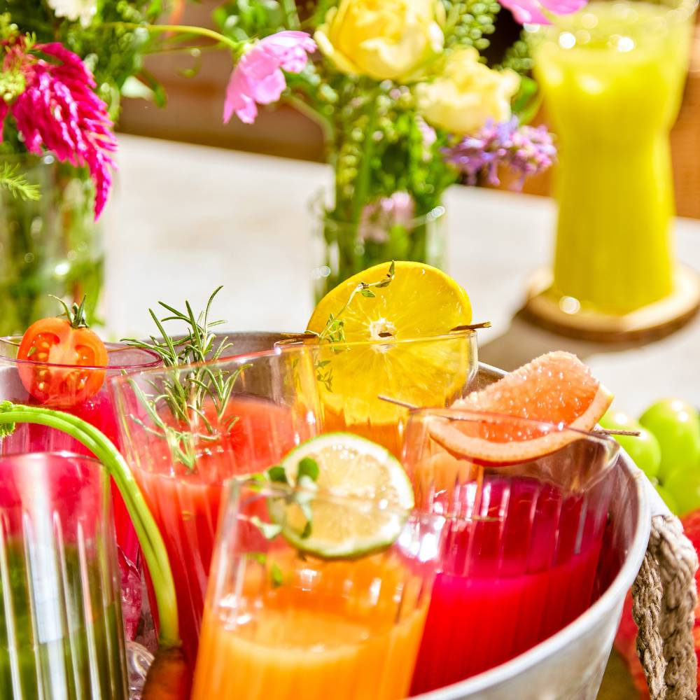 Assortimento di succhi colorati in bicchieri, guarniti con fette di frutta ed erbe.