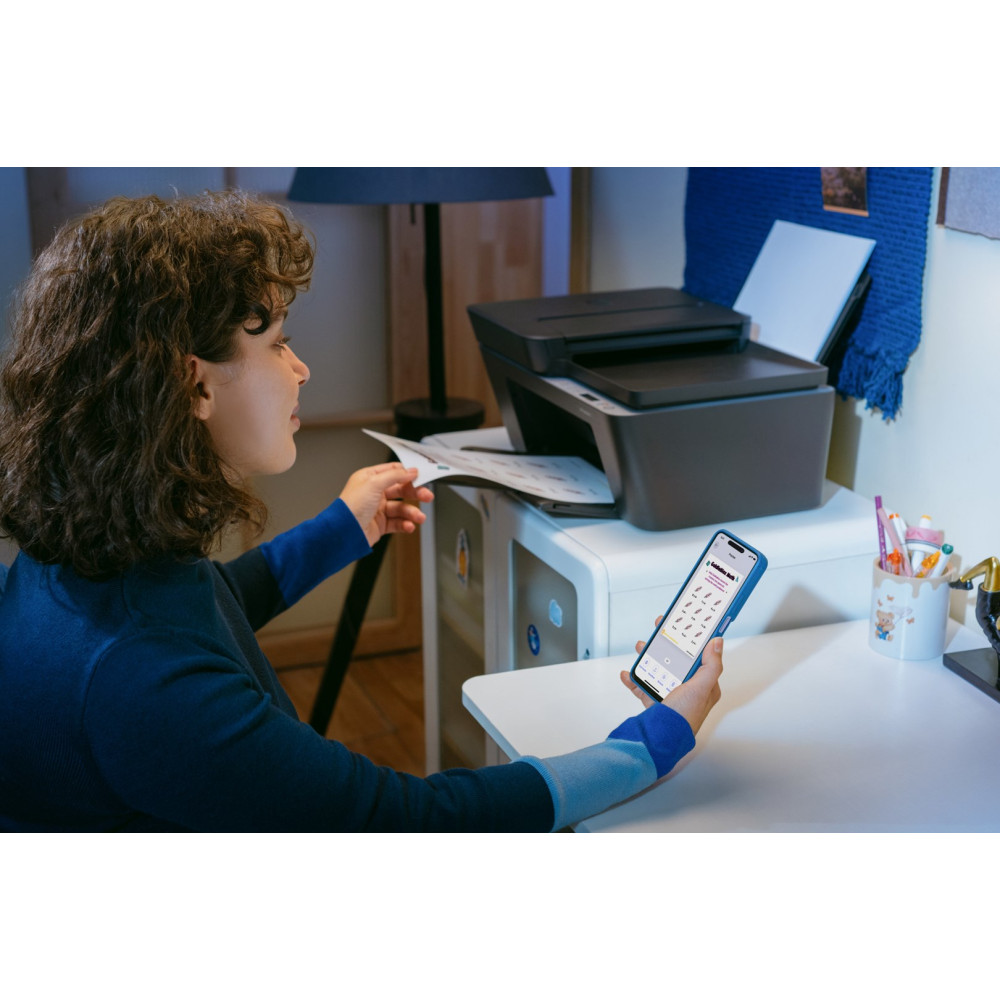 Frau mit Handy und Drucker. Sie hält ein Blatt Papier.