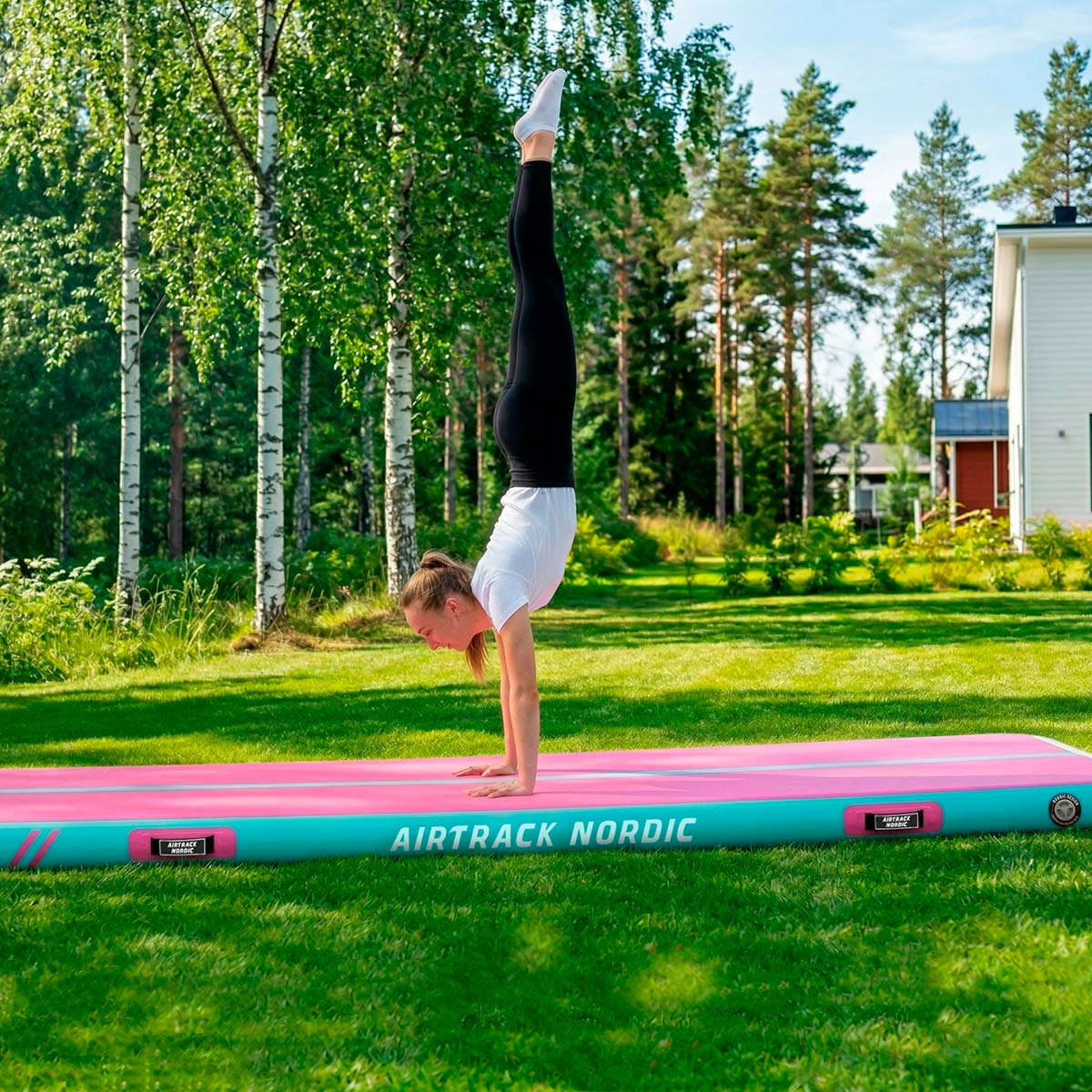 Dziewczynka robi stanie na rękach na dmuchanej macie Airtrack w ogrodzie.