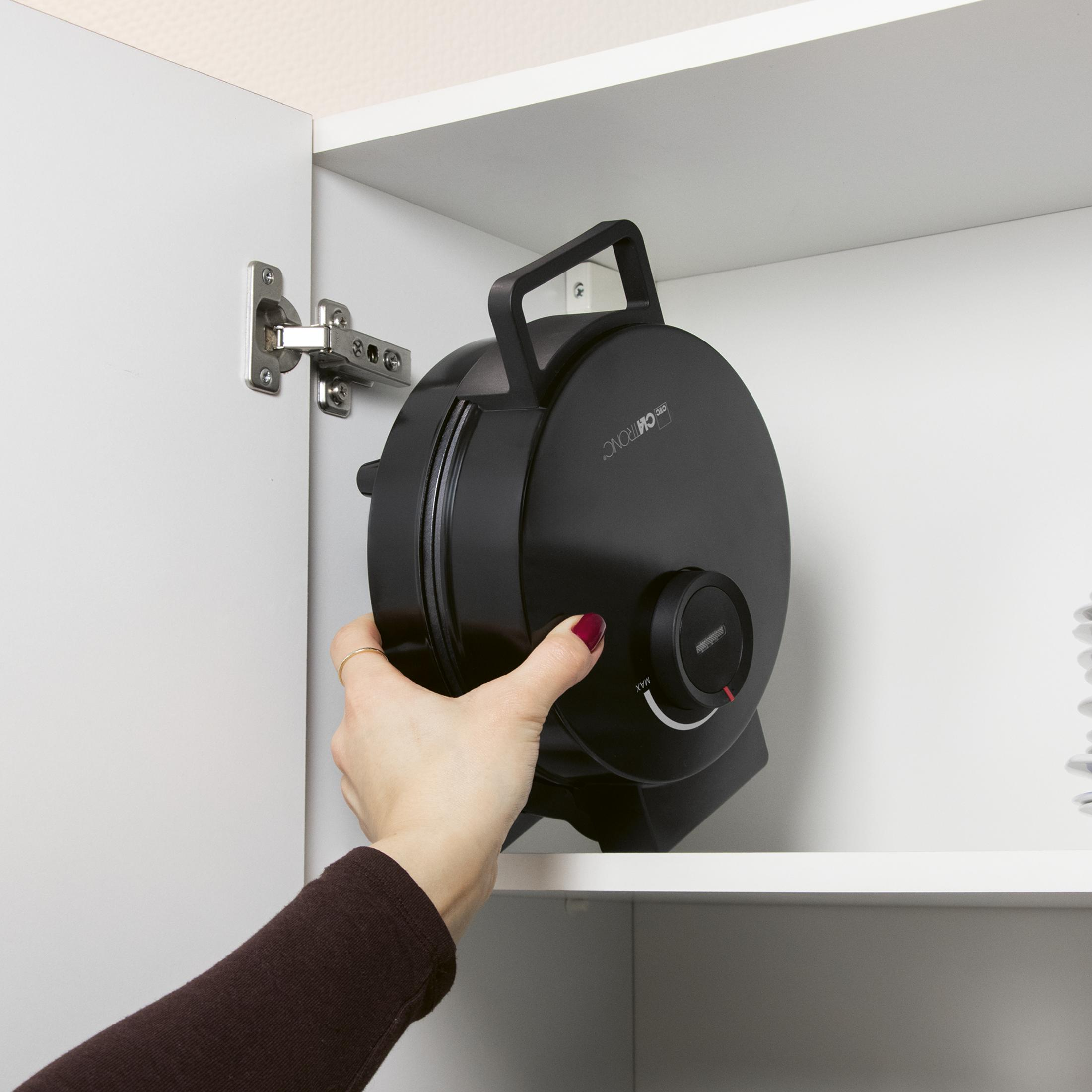 Eine Hand legt eine schwarze Waffelform in einen weißen Schrank.