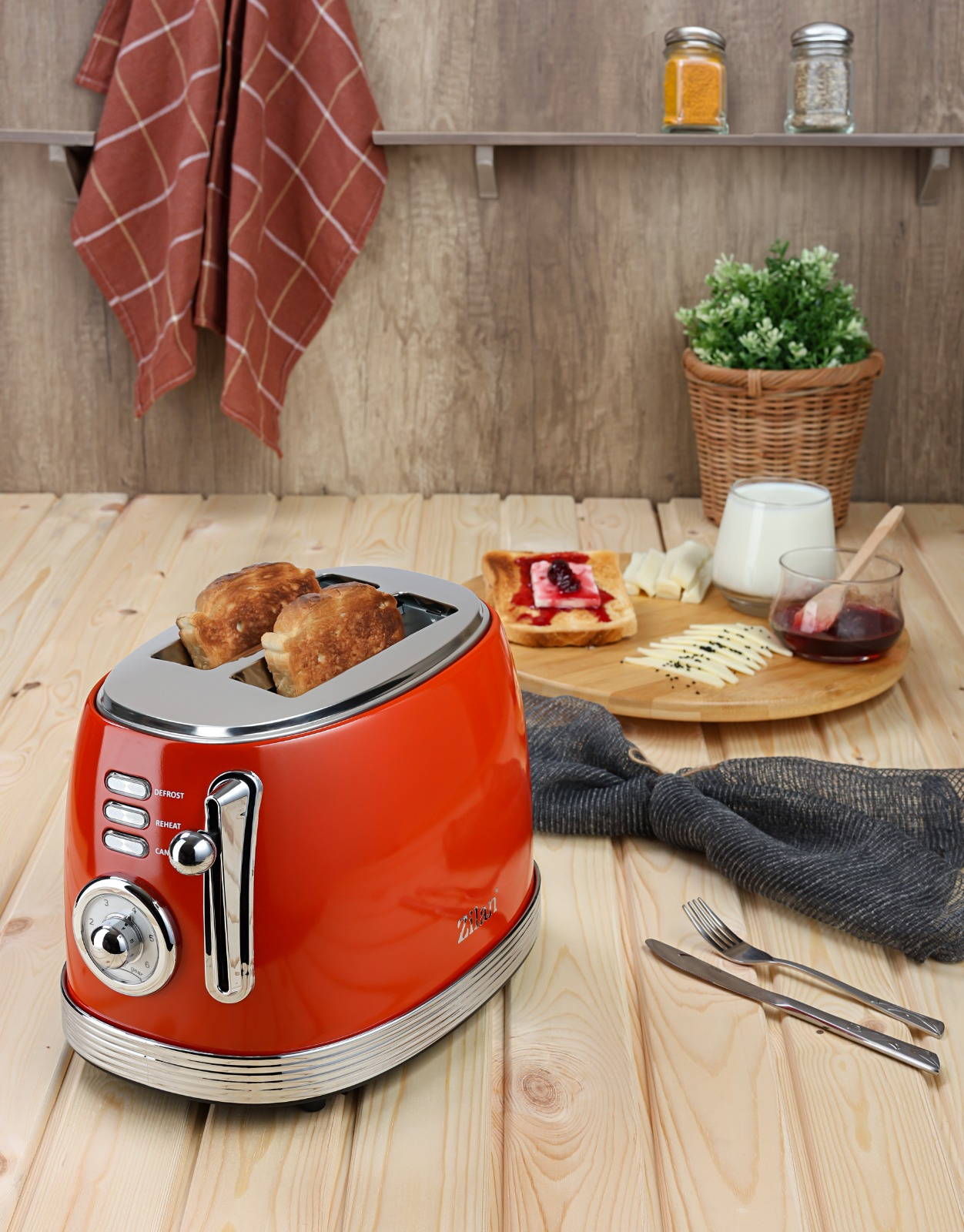 Kırmızı bir tost makinesi, üzerinde iki dilim kızarmış ekmek, yanında reçelli ekmek, peynir ve süt.
