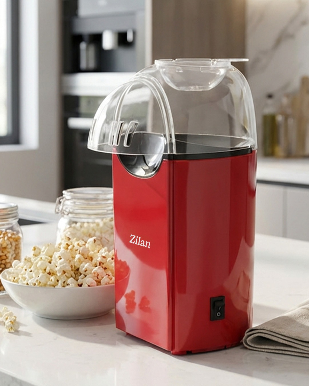 Şeffaf kapaklı kırmızı popcorn makinesi, yanında bir kase patlamış mısır.