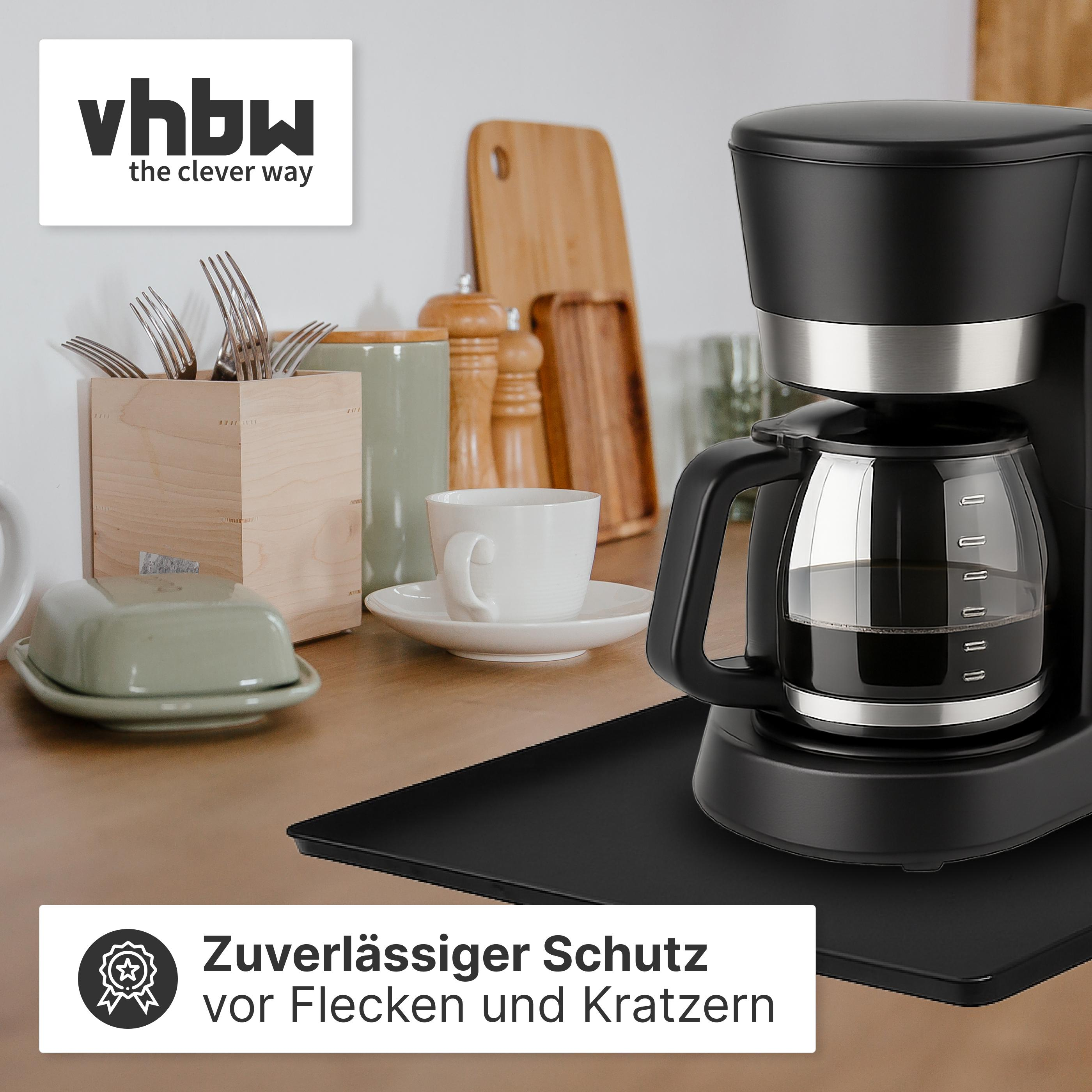 Eine schwarze Kaffeemaschine mit Glaskanne steht auf einem Tisch. Daneben sind eine Tasse und ein Buttergericht.