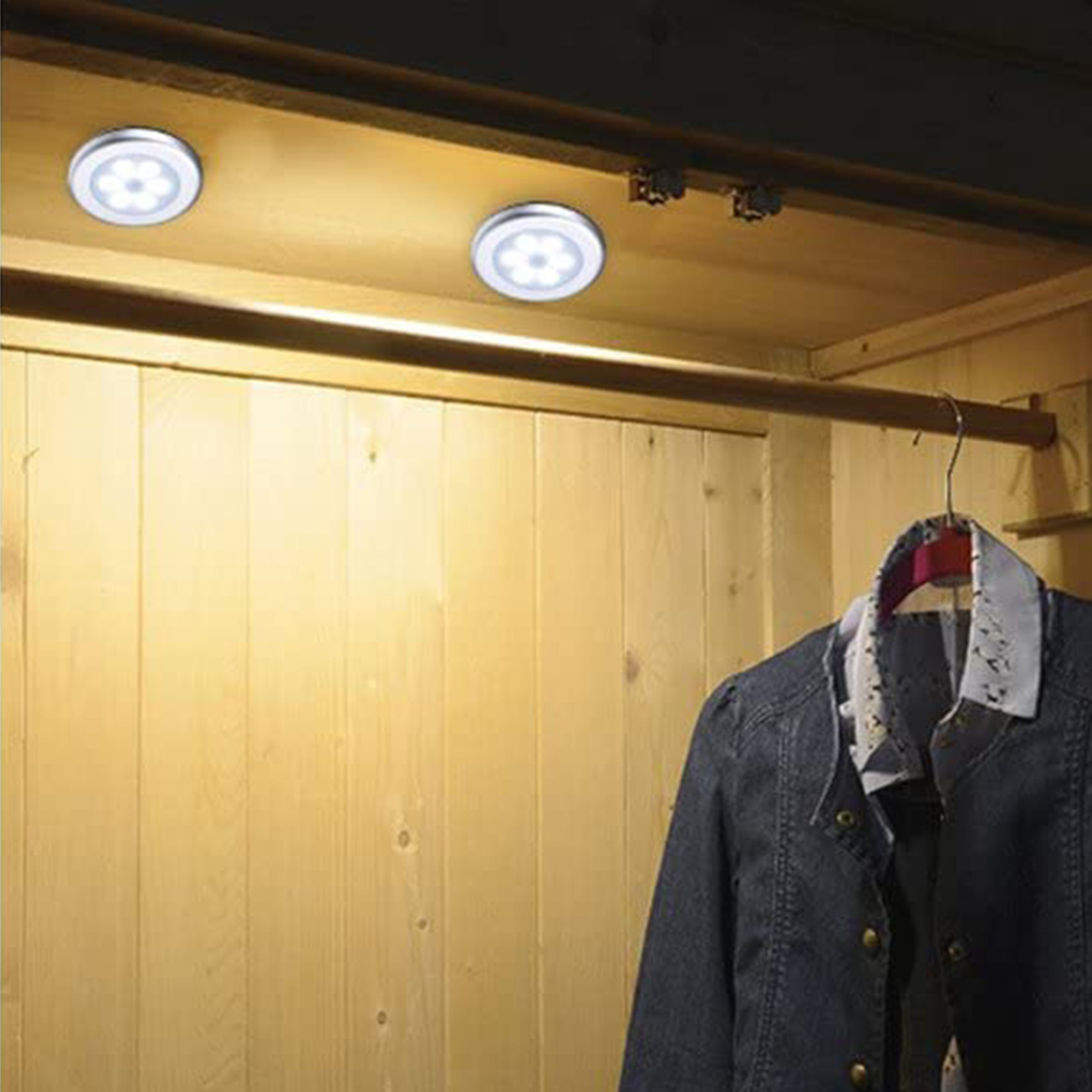 Zwei LED-Leuchten beleuchten einen Holzschrank mit Kleidung daran.
