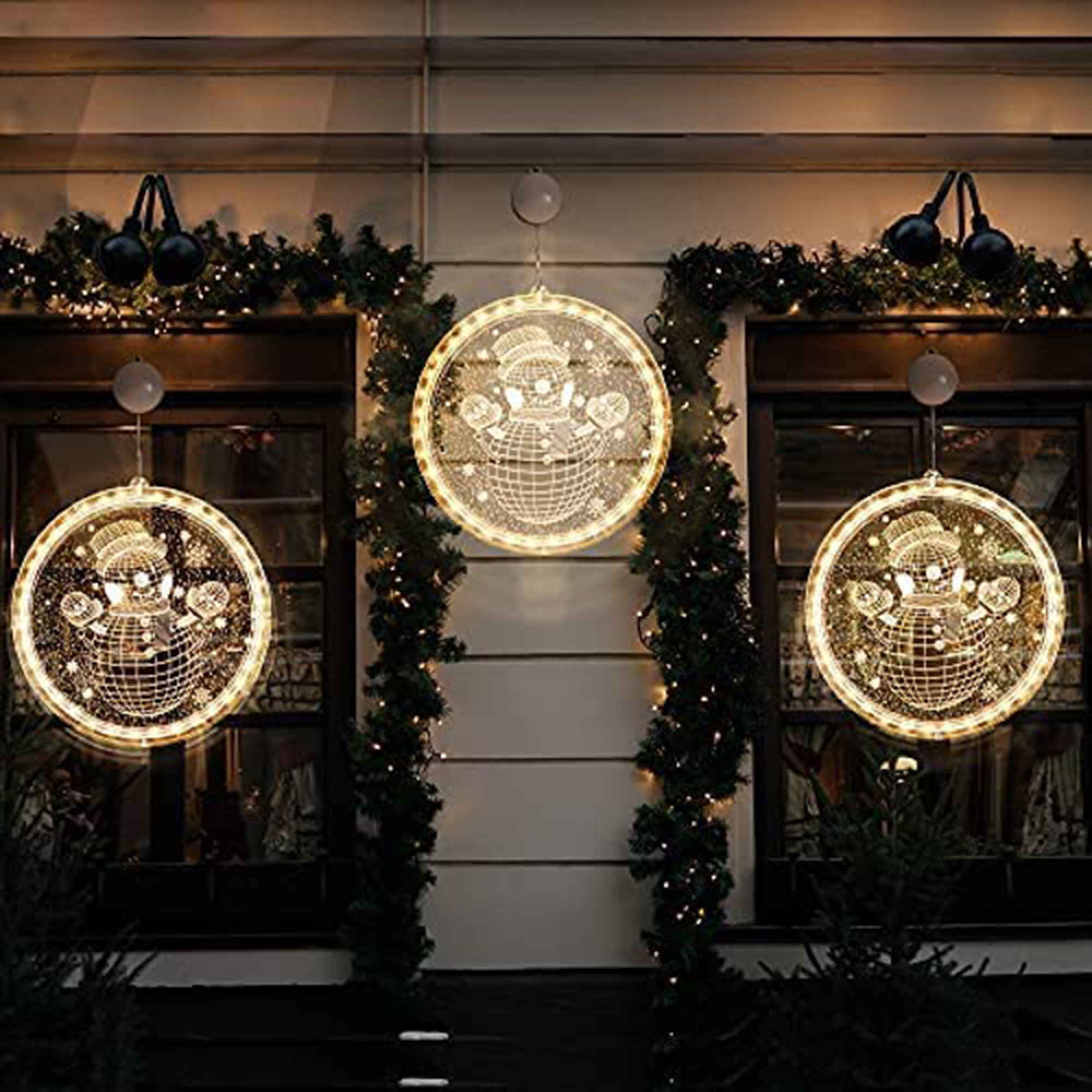 Drei leuchtende Schneemann-Fensterdekorationen hängen an einem Haus.