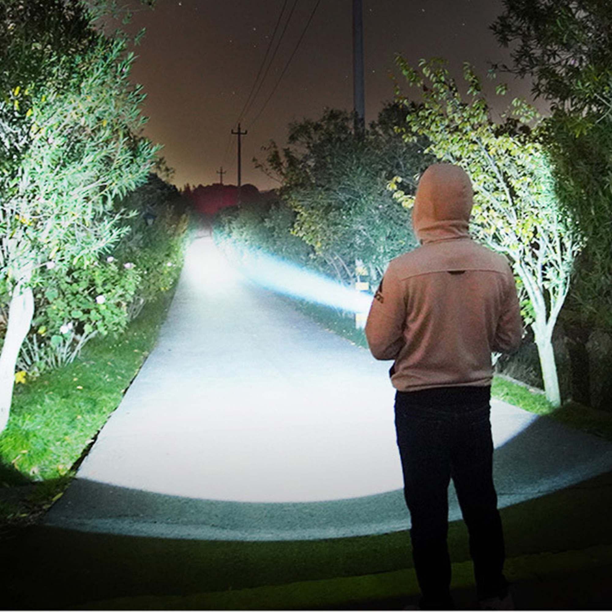 Mann mit Kapuzenpullover leuchtet mit starker Taschenlampe auf Weg im Dunkeln.