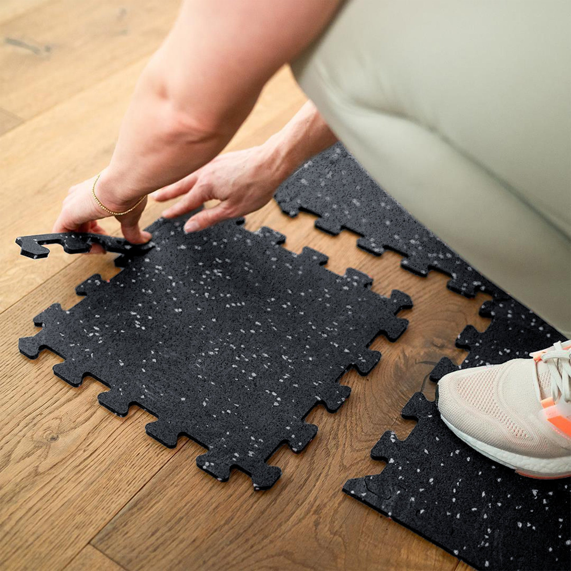 Hände legen schwarze Puzzlematten auf Holzboden.