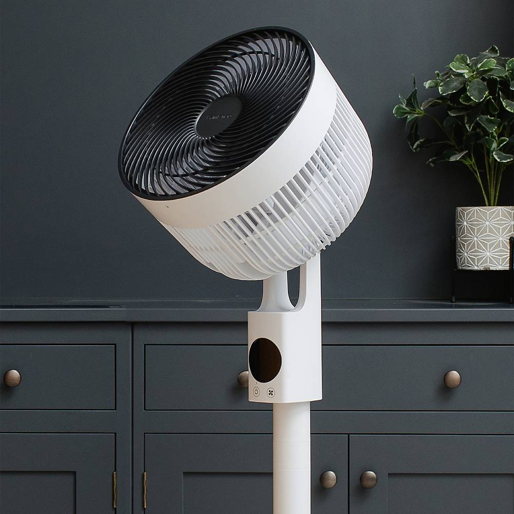 Ein weißer Standventilator mit schwarzem Gitter steht auf einem dunklen Schrank.