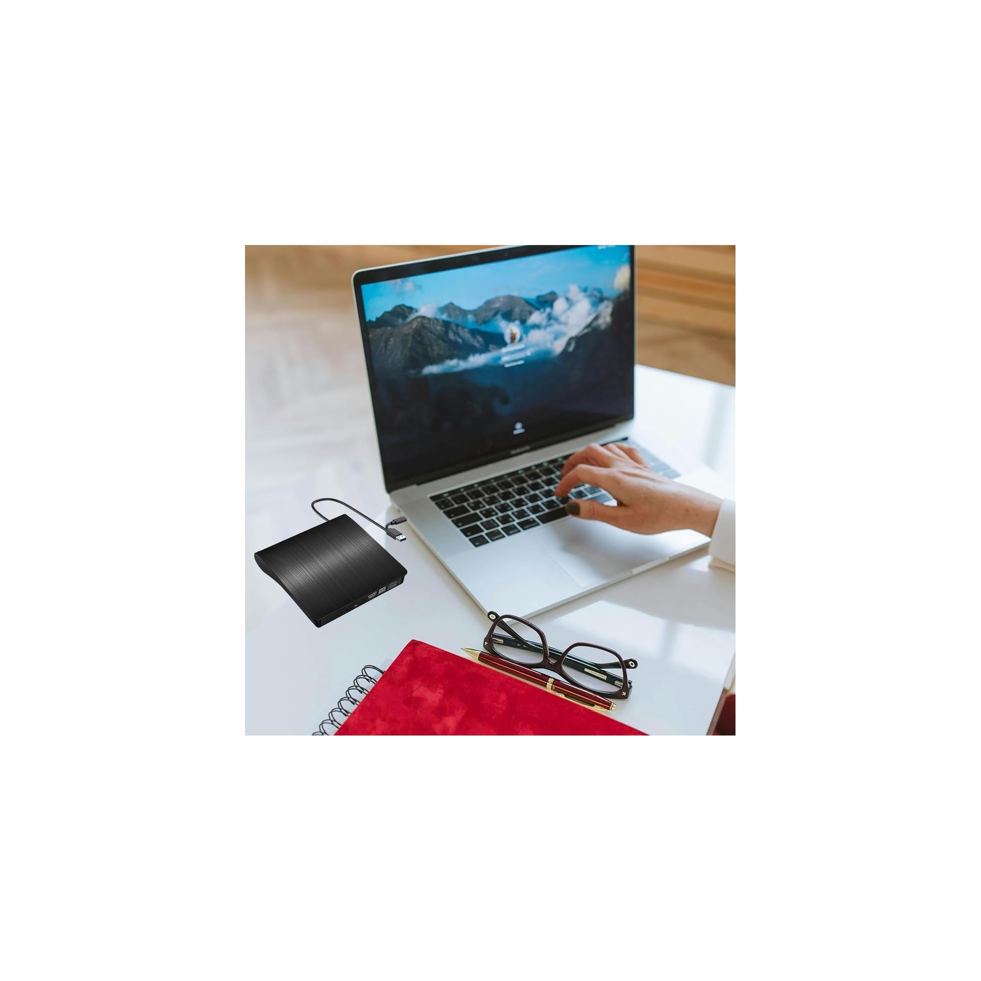 Schwarzer externer DVD-Brenner neben einem Laptop, Notizbuch und Brille.