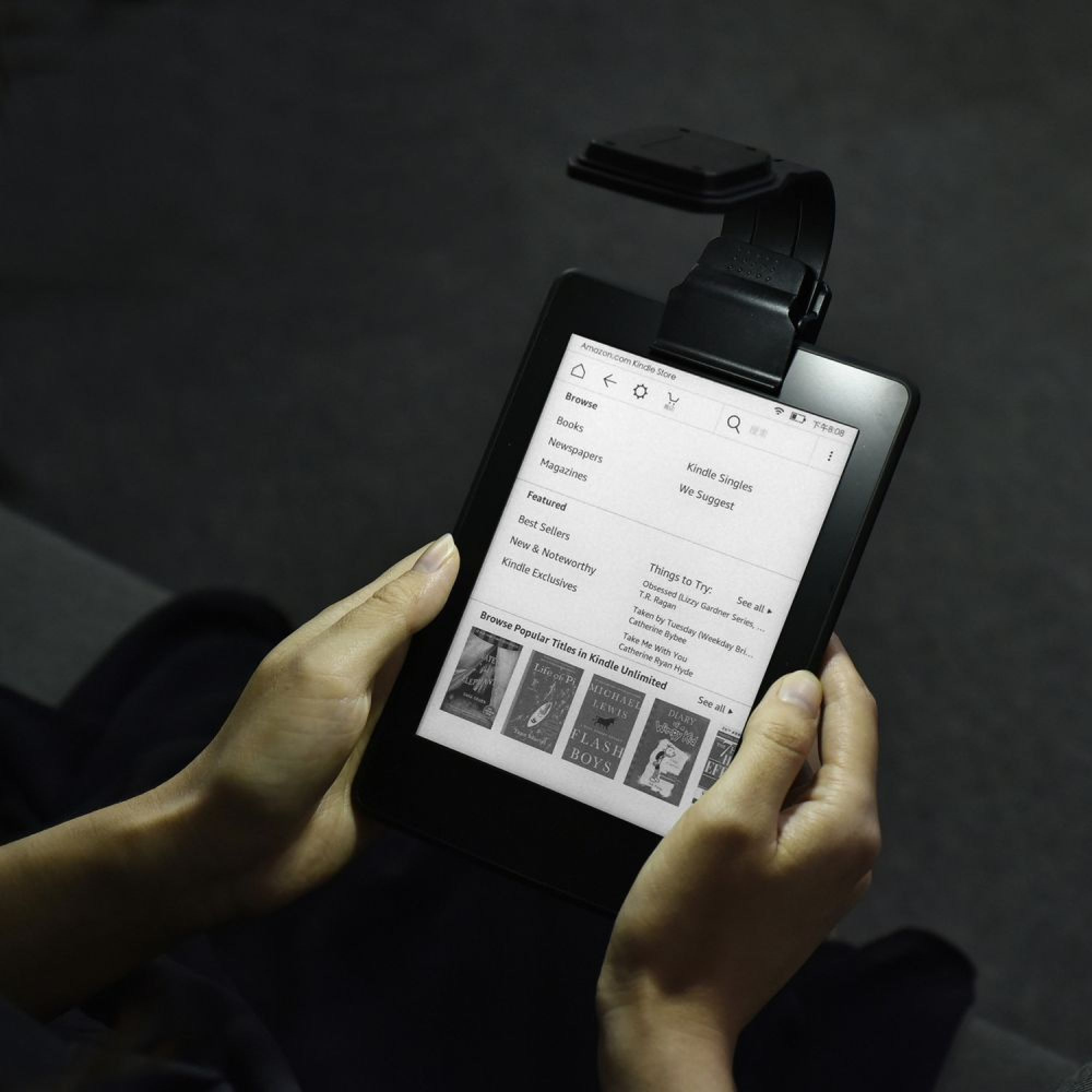 Eine Person hält ein Kindle-Gerät mit einem Buchladen-Bildschirm und einer Leselampe.