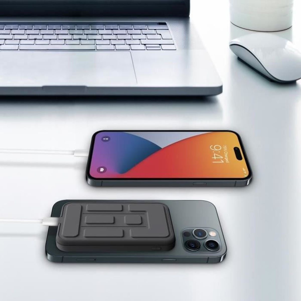 Eine graue Powerbank ist an einem Handy befestigt, das ein anderes Handy auflädt, neben einem Laptop.