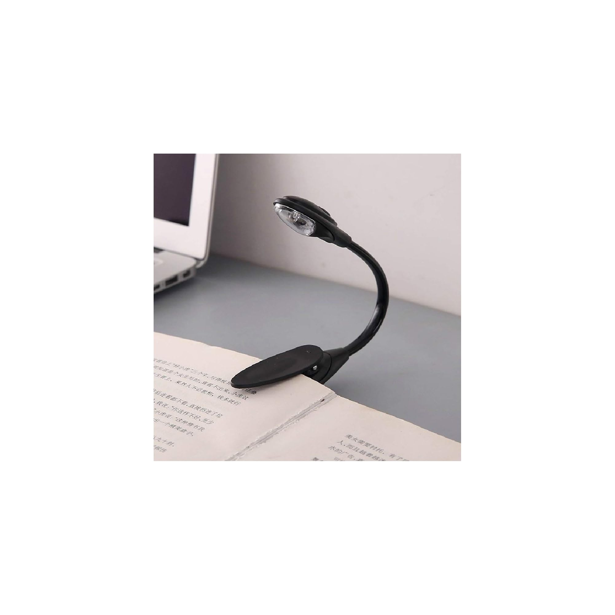 Ein schwarzes Clip-On-Leselicht beleuchtet ein offenes Buch neben einem Laptop.