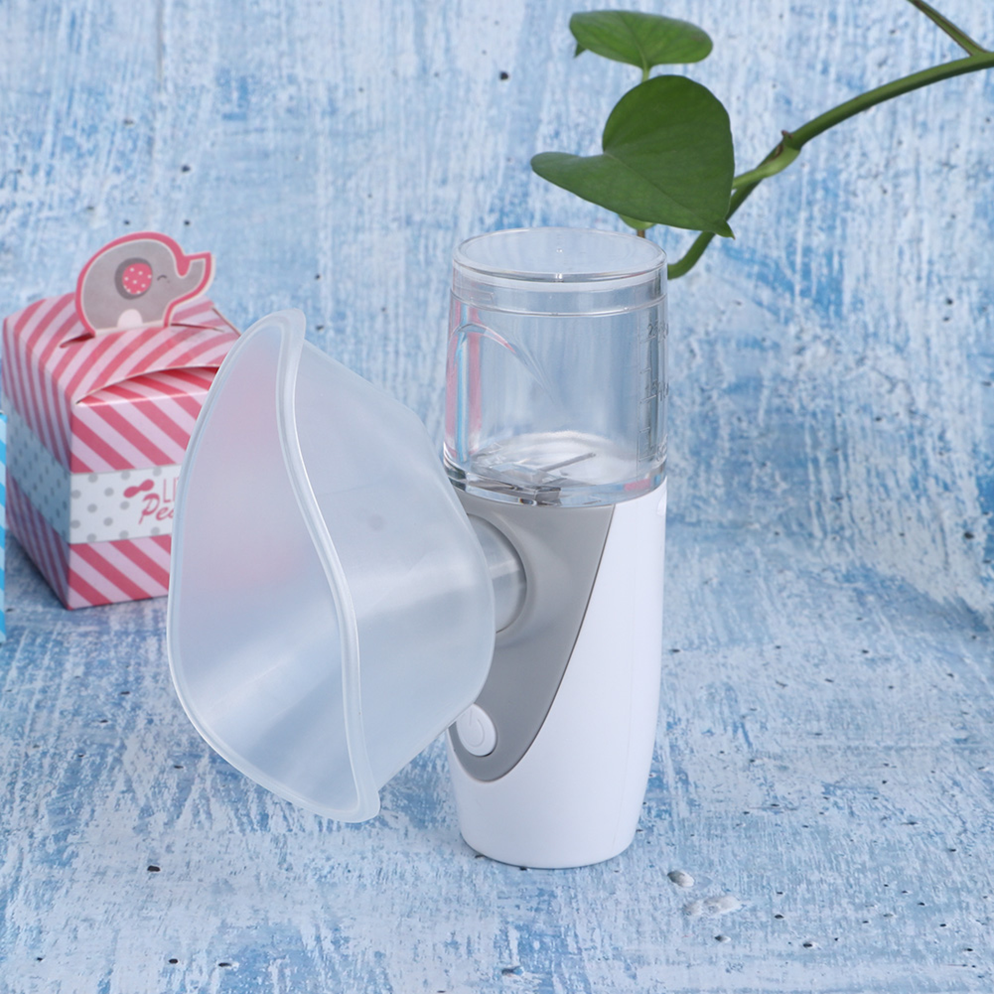 Ein weißer Vernebler mit durchsichtigem Behälter steht neben einer rosa gestreiften Box.