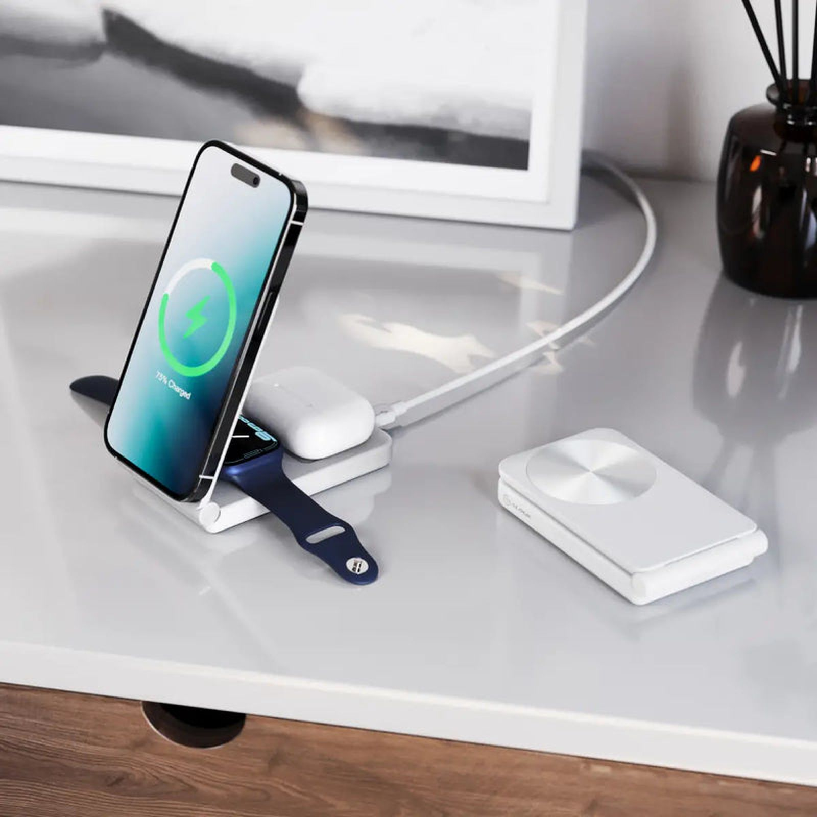 Ein Smartphone, eine Smartwatch und Ohrhörer laden auf einem weißen Ladegerät.