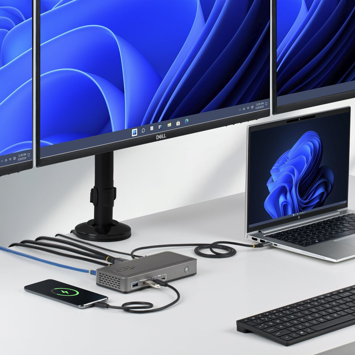 Mehrere Monitore, Laptop, Dockingstation, Smartphone und Tastatur auf einem Schreibtisch.