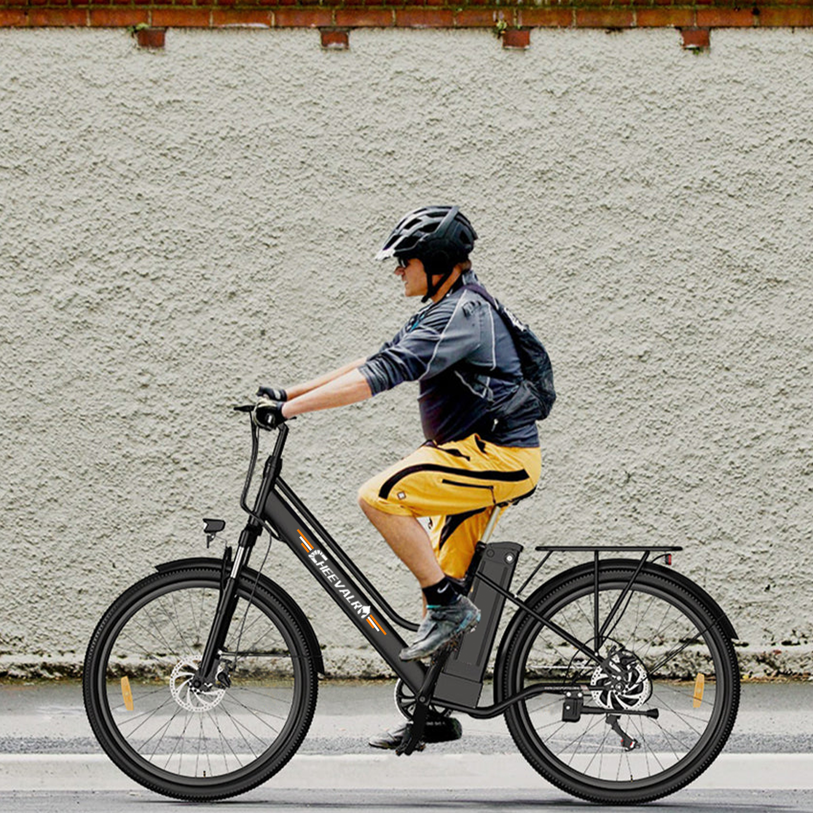 Ein Mann mit Helm fährt ein schwarzes E-Bike vor einer rauen Mauer.