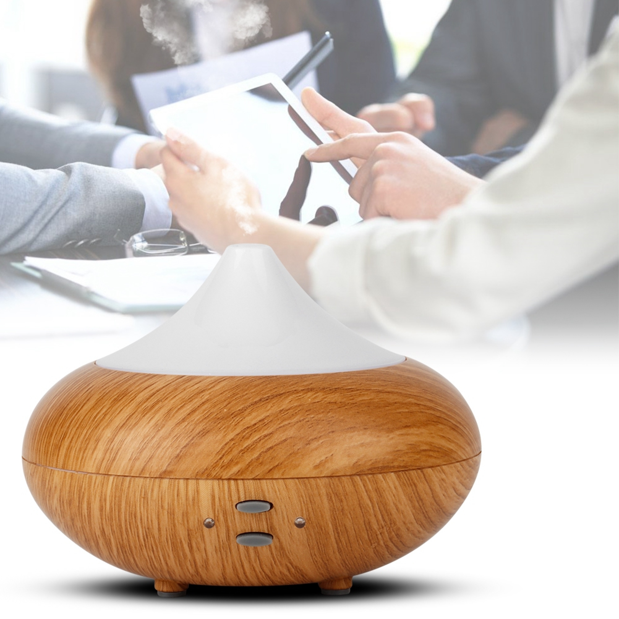 Ein Holzmaserung-Diffusor mit weißem Deckel gibt Dampf ab, während im Hintergrund Menschen arbeiten.