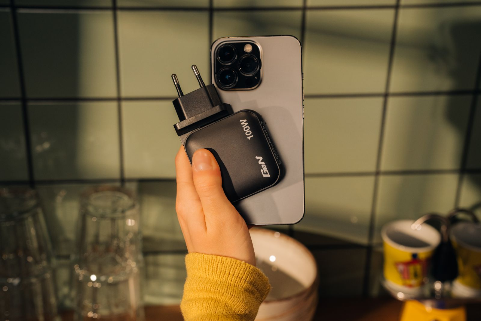 Eine Hand hält ein schwarzes Ladegerät mit 100W und ein graues Smartphone.