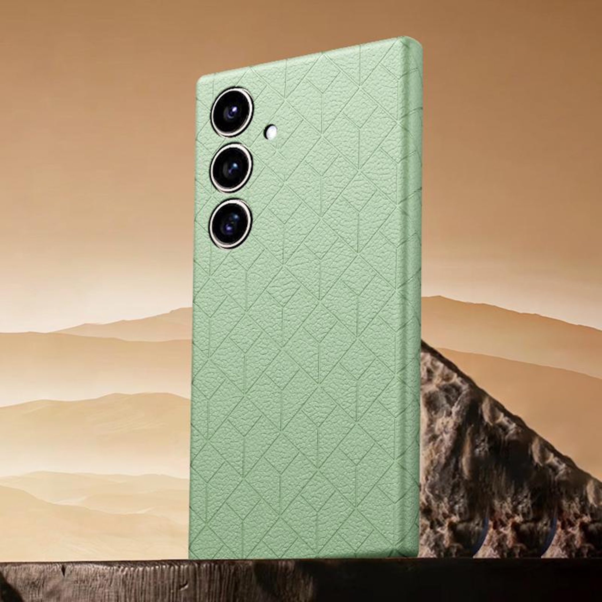 Un teléfono verde claro con tres cámaras sobre una viga de madera frente a un paisaje desértico.