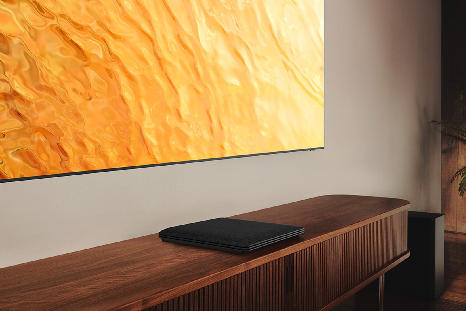 Un altoparlante nero poggia su un mobile in legno davanti a una TV con immagine gialla.