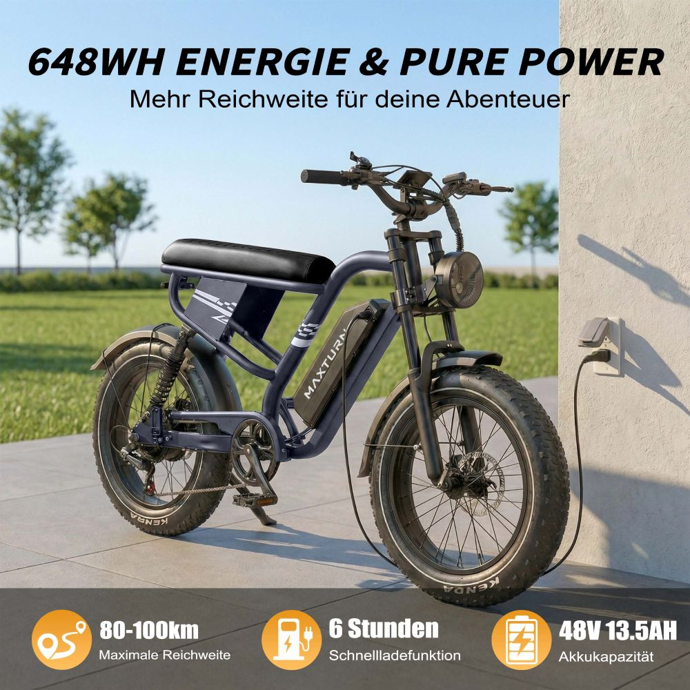 Bicicleta eléctrica azul oscuro con ruedas anchas, enchufada para cargar. Autonomía 80-100 km.