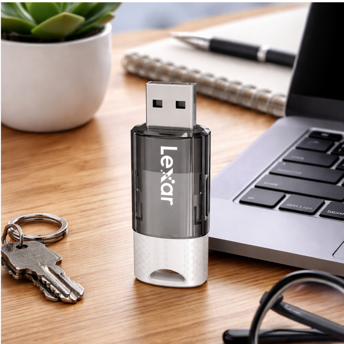 Una unidad USB Lexar está sobre un escritorio de madera junto a llaves y un portátil.